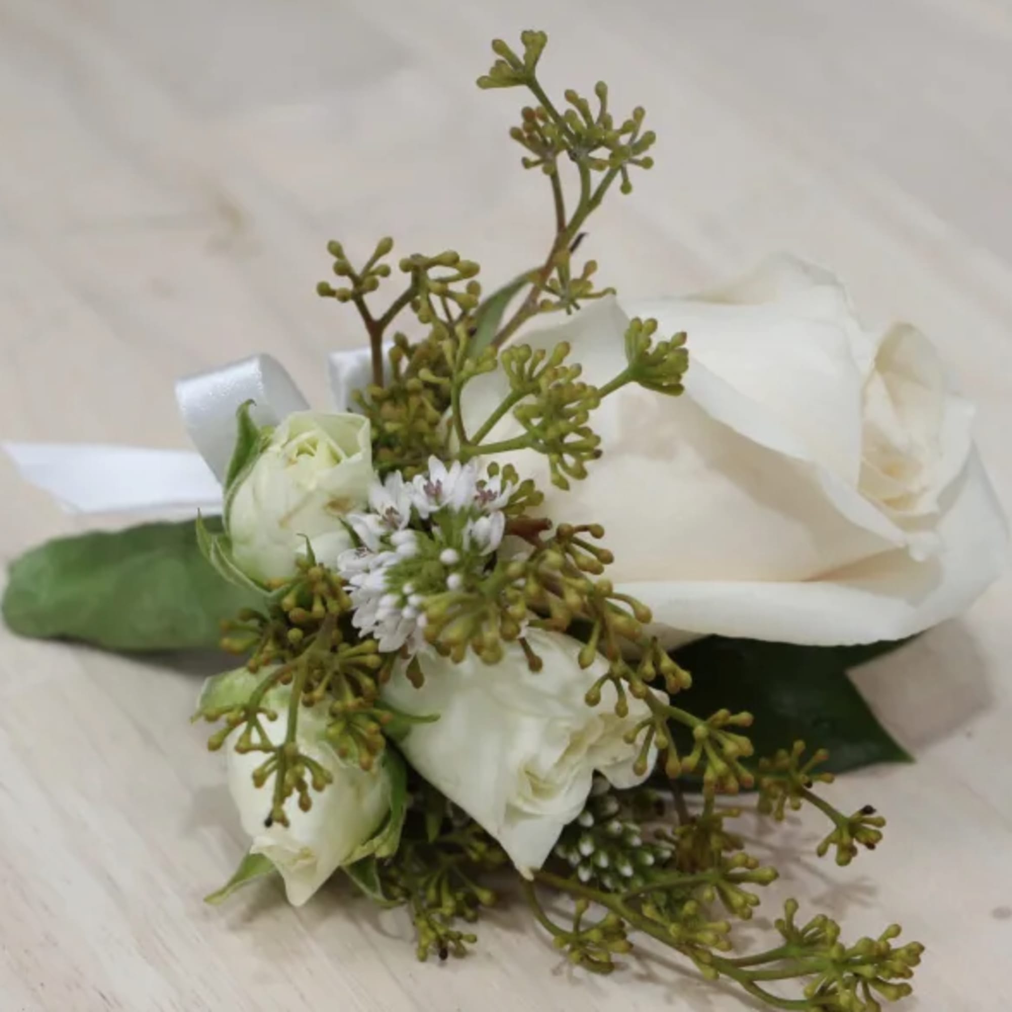 White rose boutonniere with small white filler flowers, buds, and a white ribbon tie