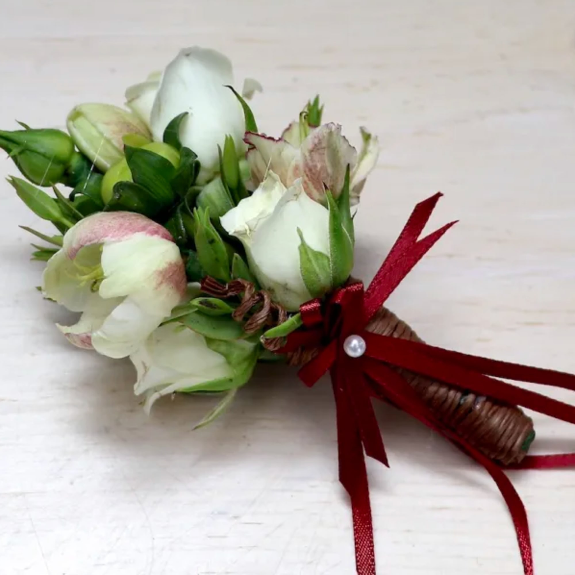 Small white rosebud boutonniere wrapped in brown twine with a red ribbon bow.