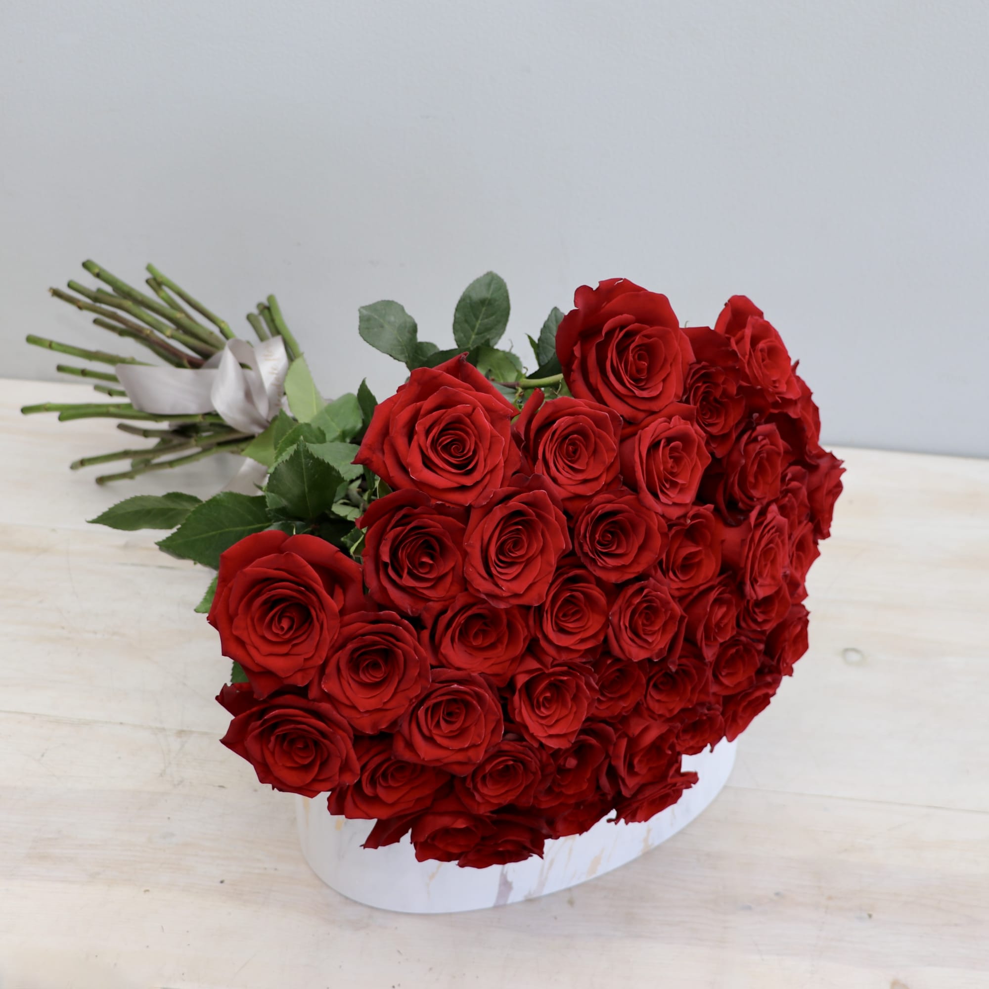 Large cluster of red roses in a low white container with stems tied by a ribbon.