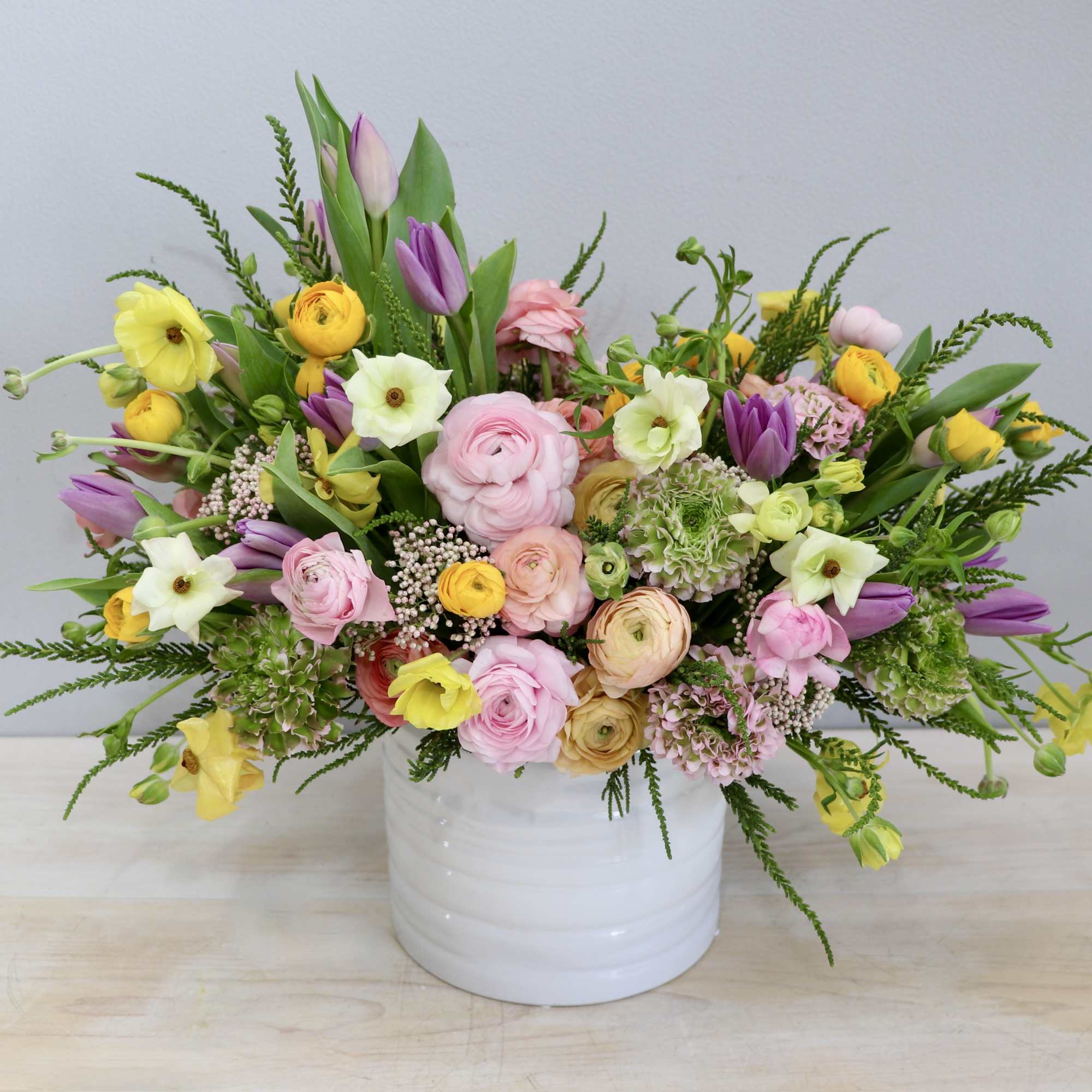 Low white vase overflowing with pink, yellow, and purple spring flowers in a loose arrangement
