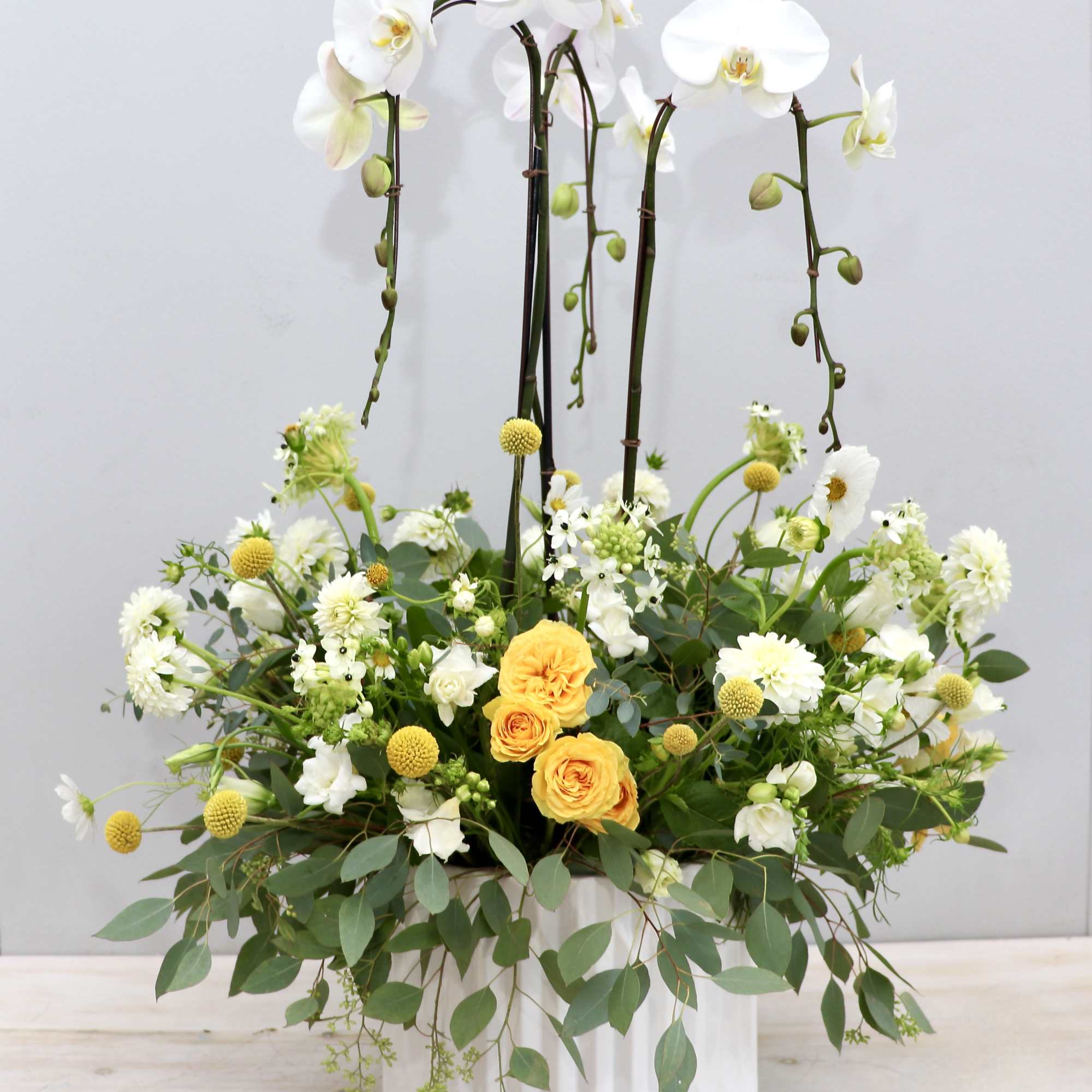 Tall white orchid planter with yellow roses and white flowers in a white ceramic pot