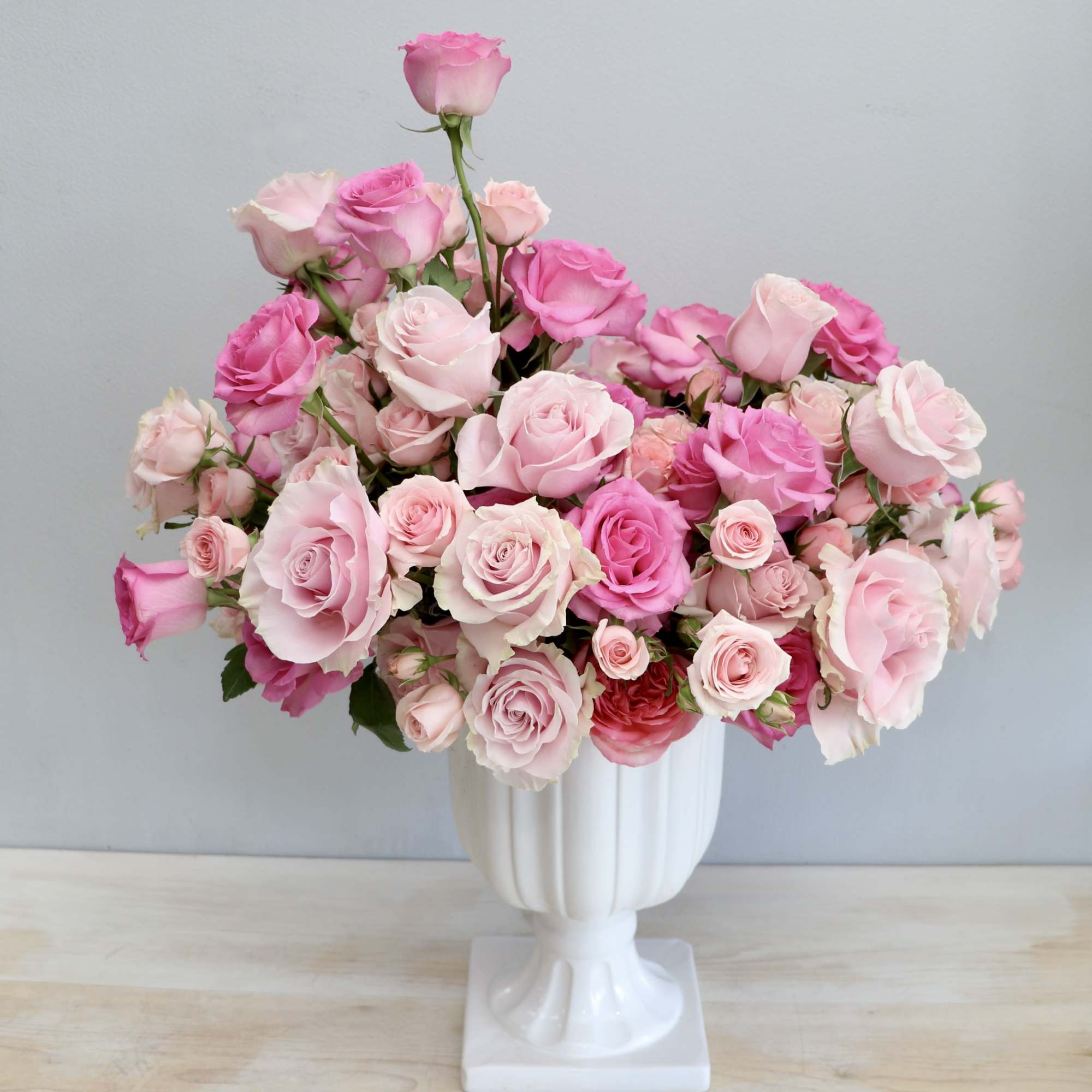 Large arrangement of light and hot pink roses in a white pedestal vase