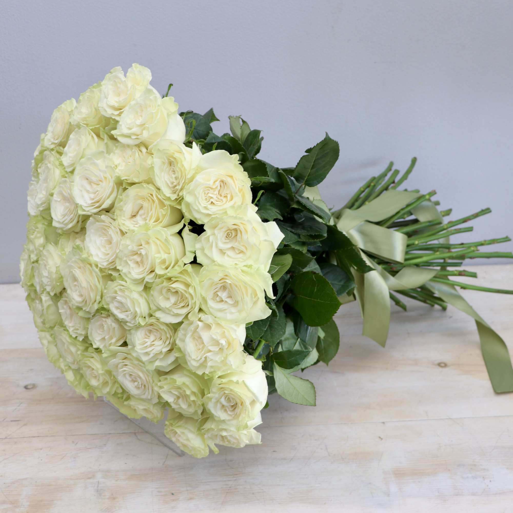 Large hand-tied bouquet of pale cream roses bound with a light green ribbon