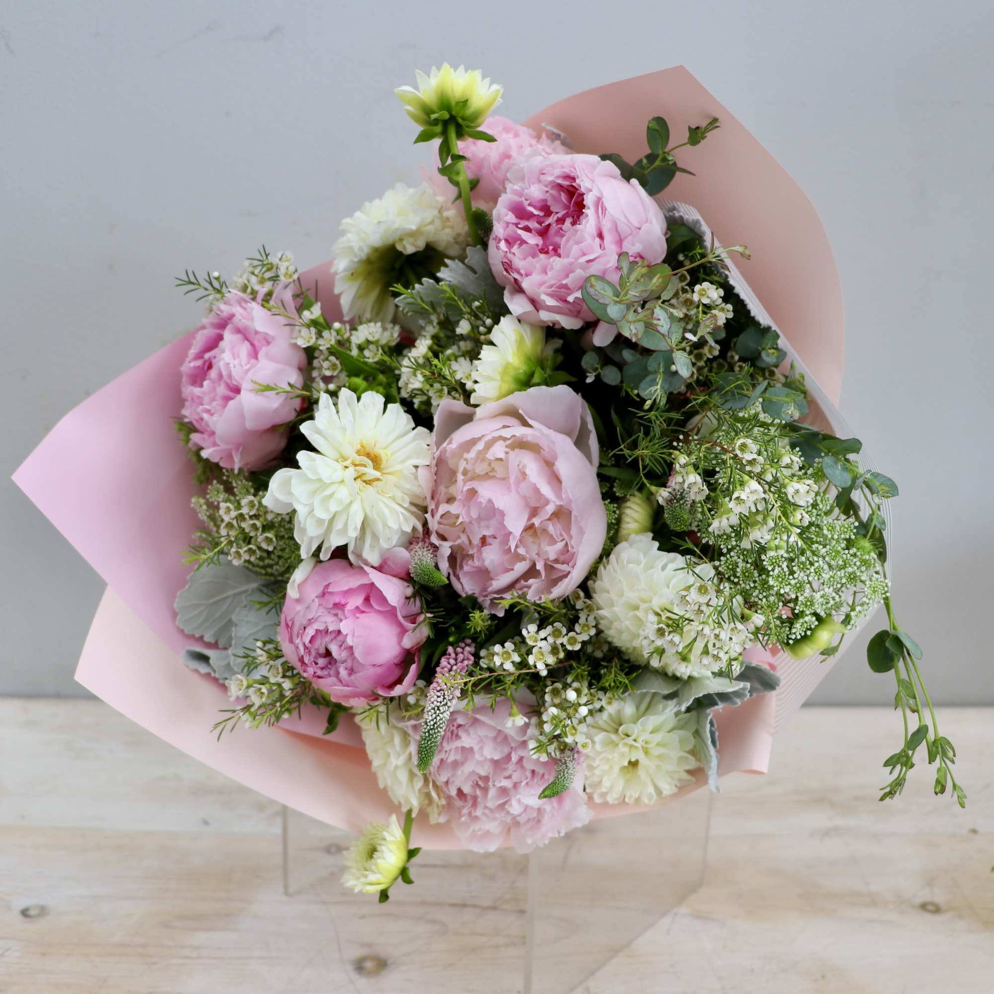 Hand-tied bouquet of pink peonies and white flowers wrapped in pale pink paper