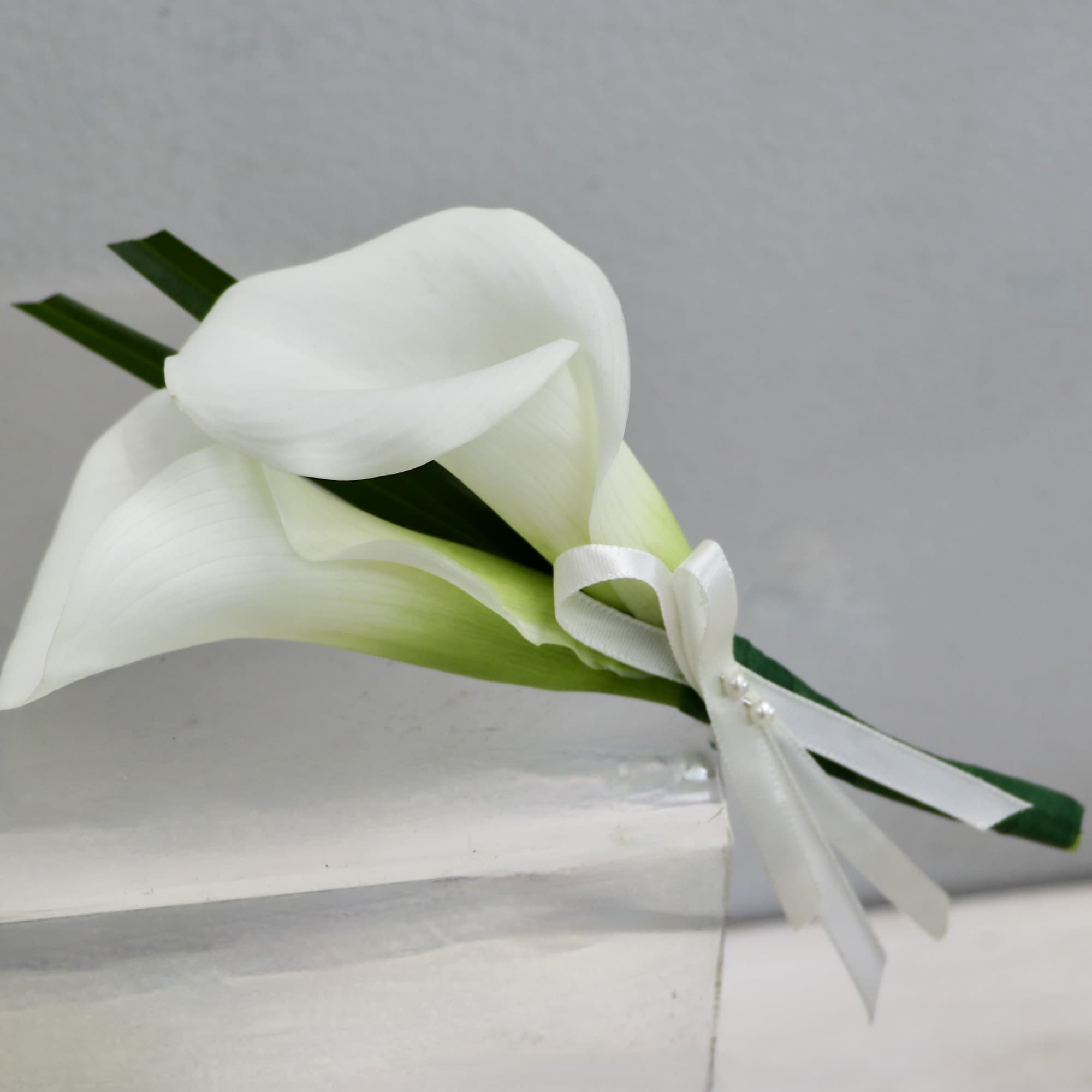 White calla lily boutonniere with ribbon and greenery blades