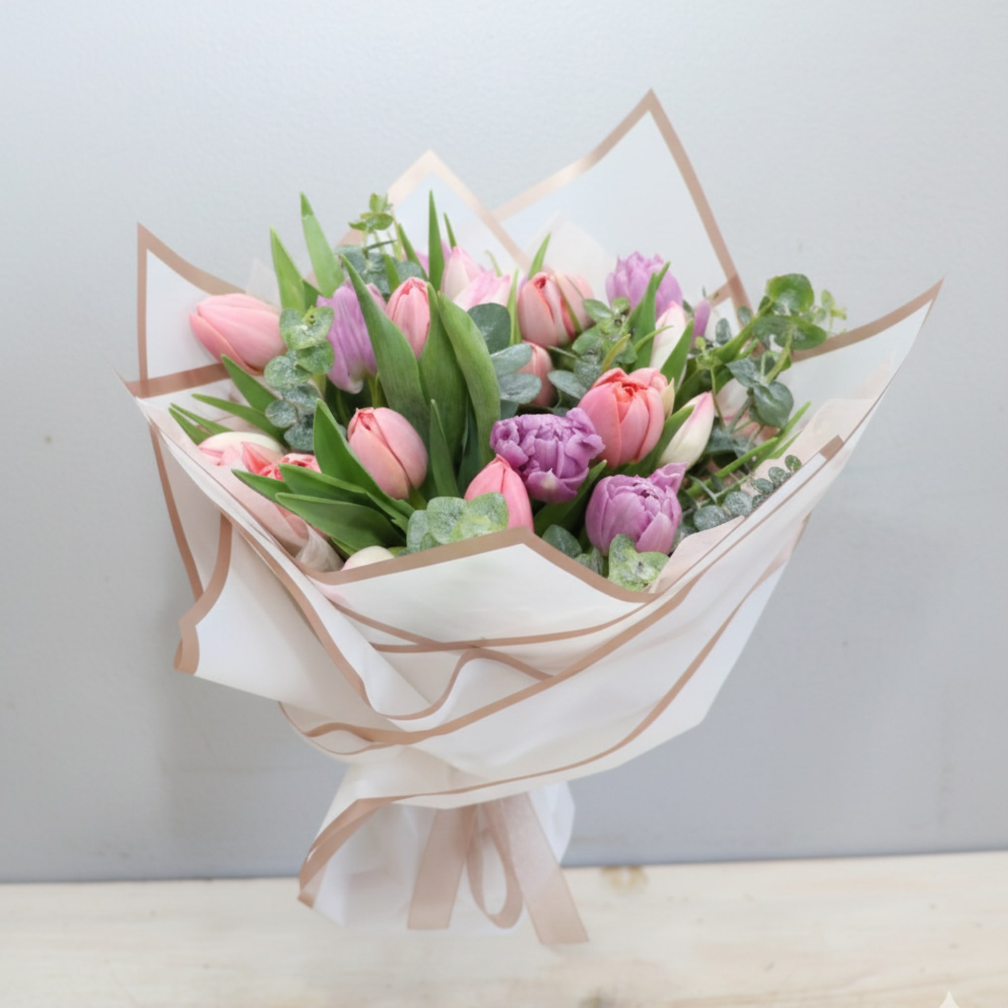 Hand-tied bouquet of pink and purple tulips wrapped in white paper with ribbon