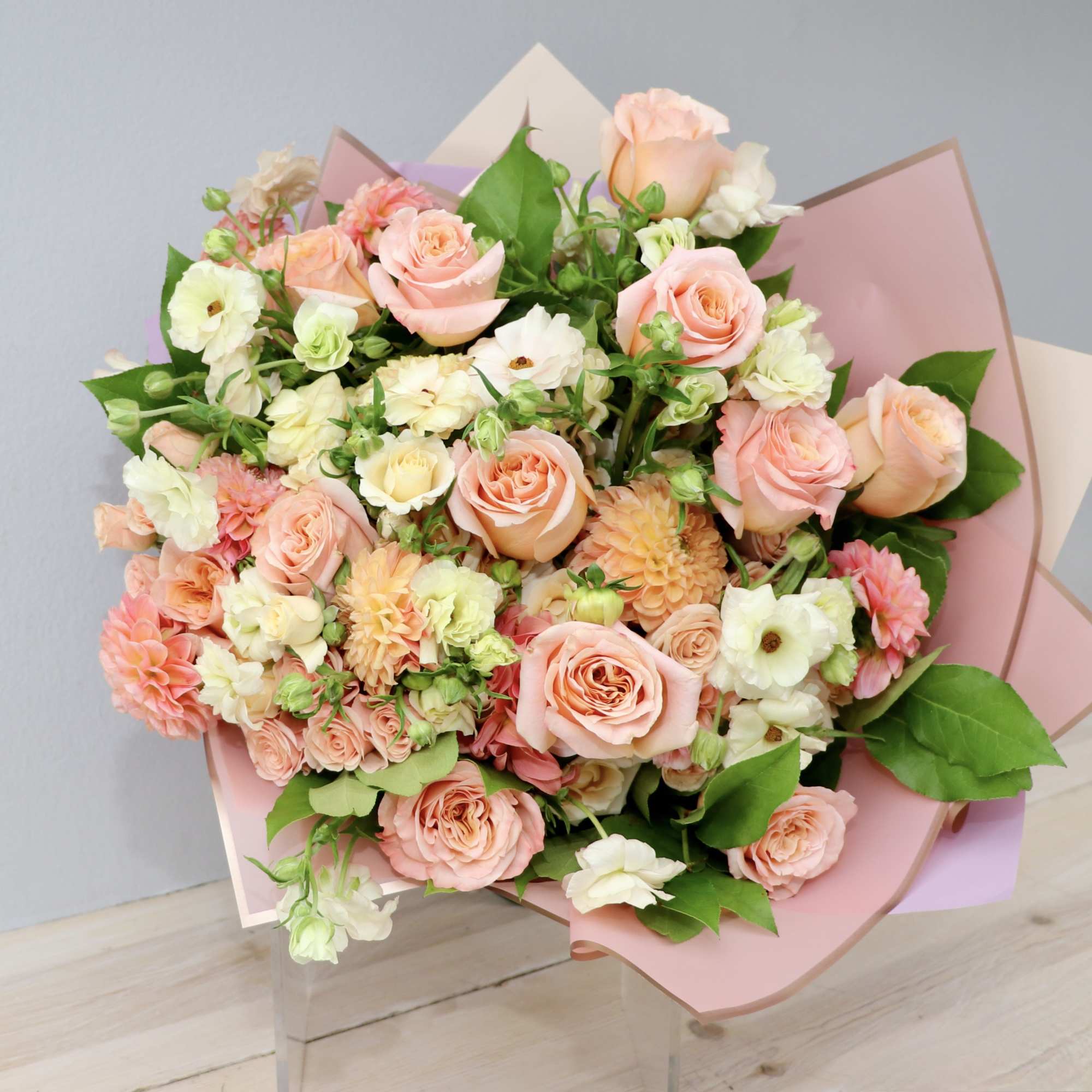Bouquet of peach and white roses with mixed blooms wrapped in pink paper