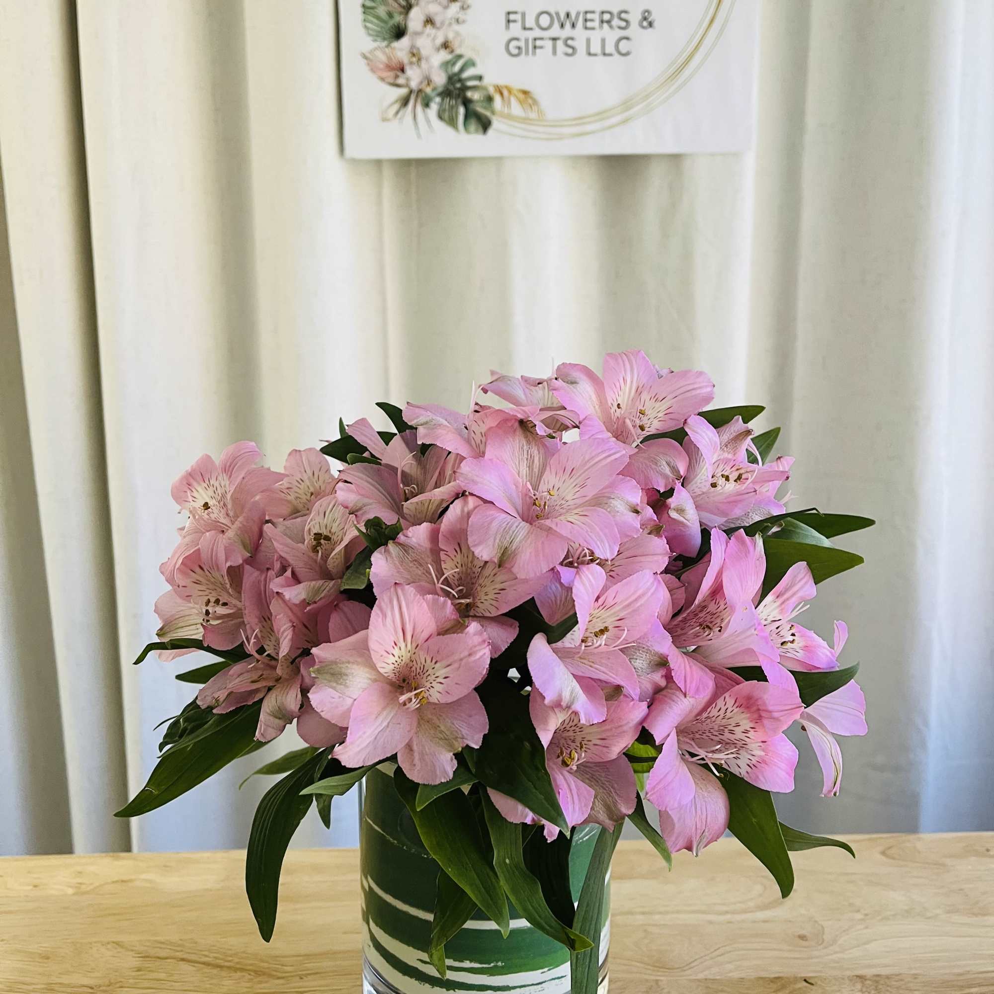 Compact bouquet of pink alstroemeria in a clear glass cylinder vase on a wooden table.