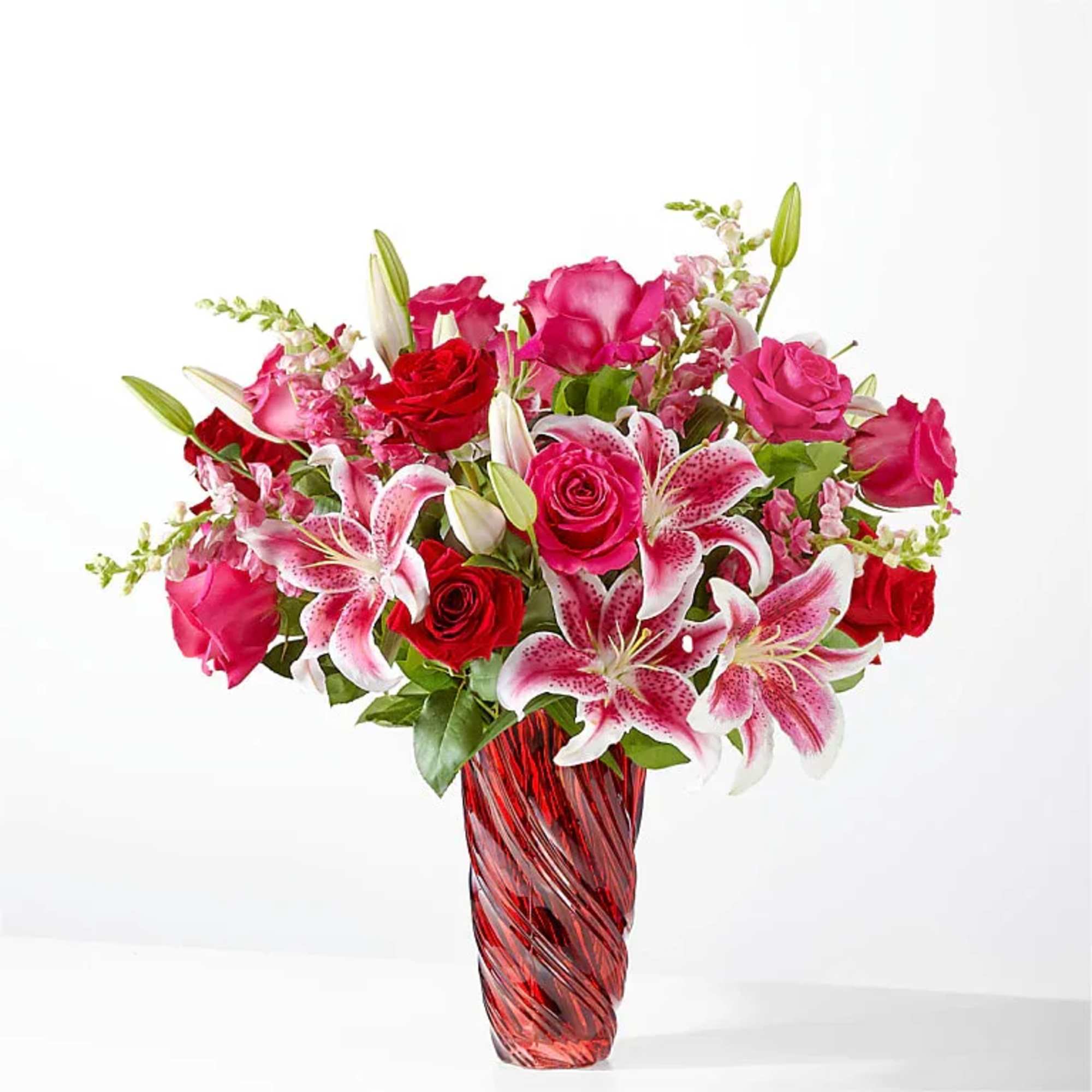Pink and red roses with lilies in a red glass vase