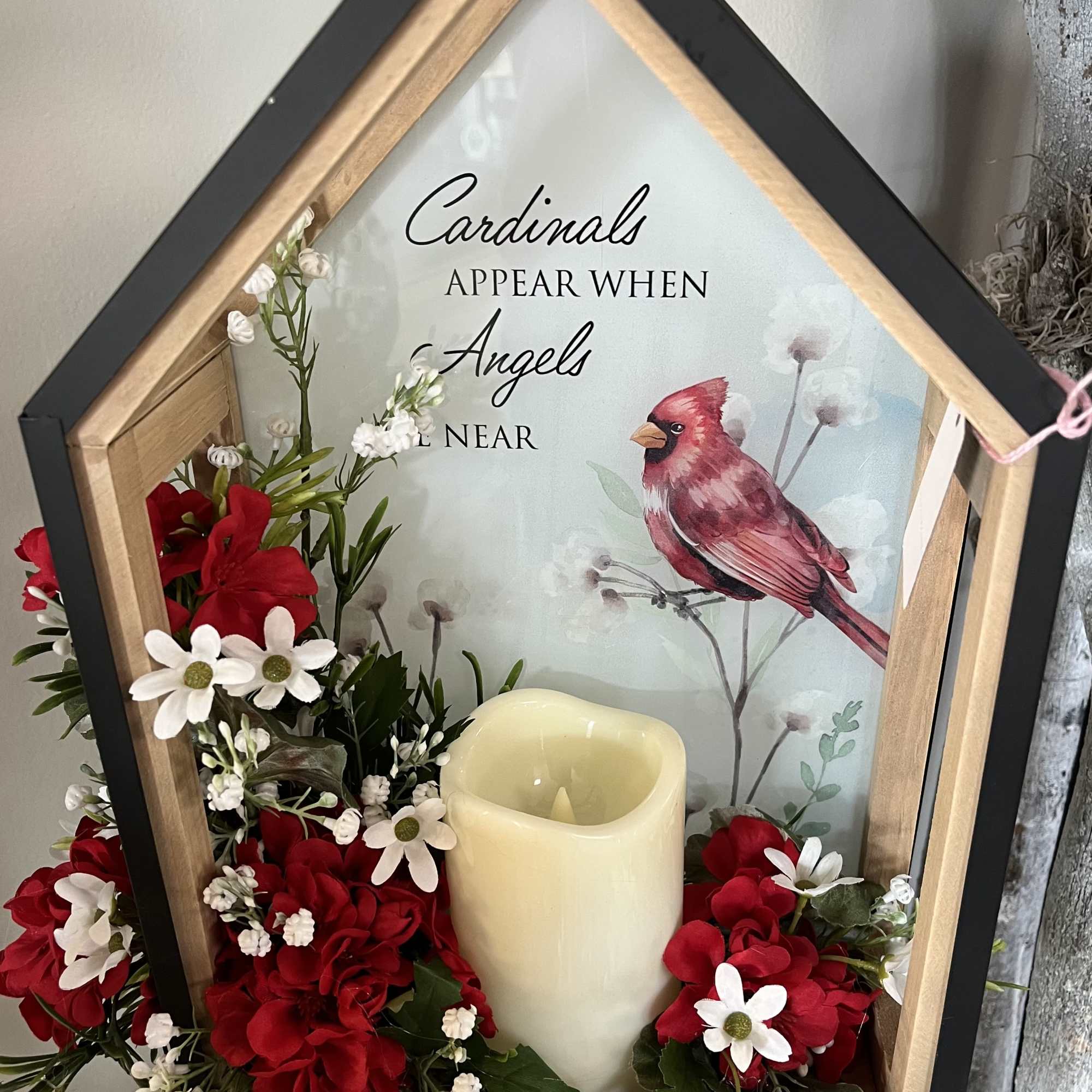 Framed memorial sign with red and white flowers and a candle