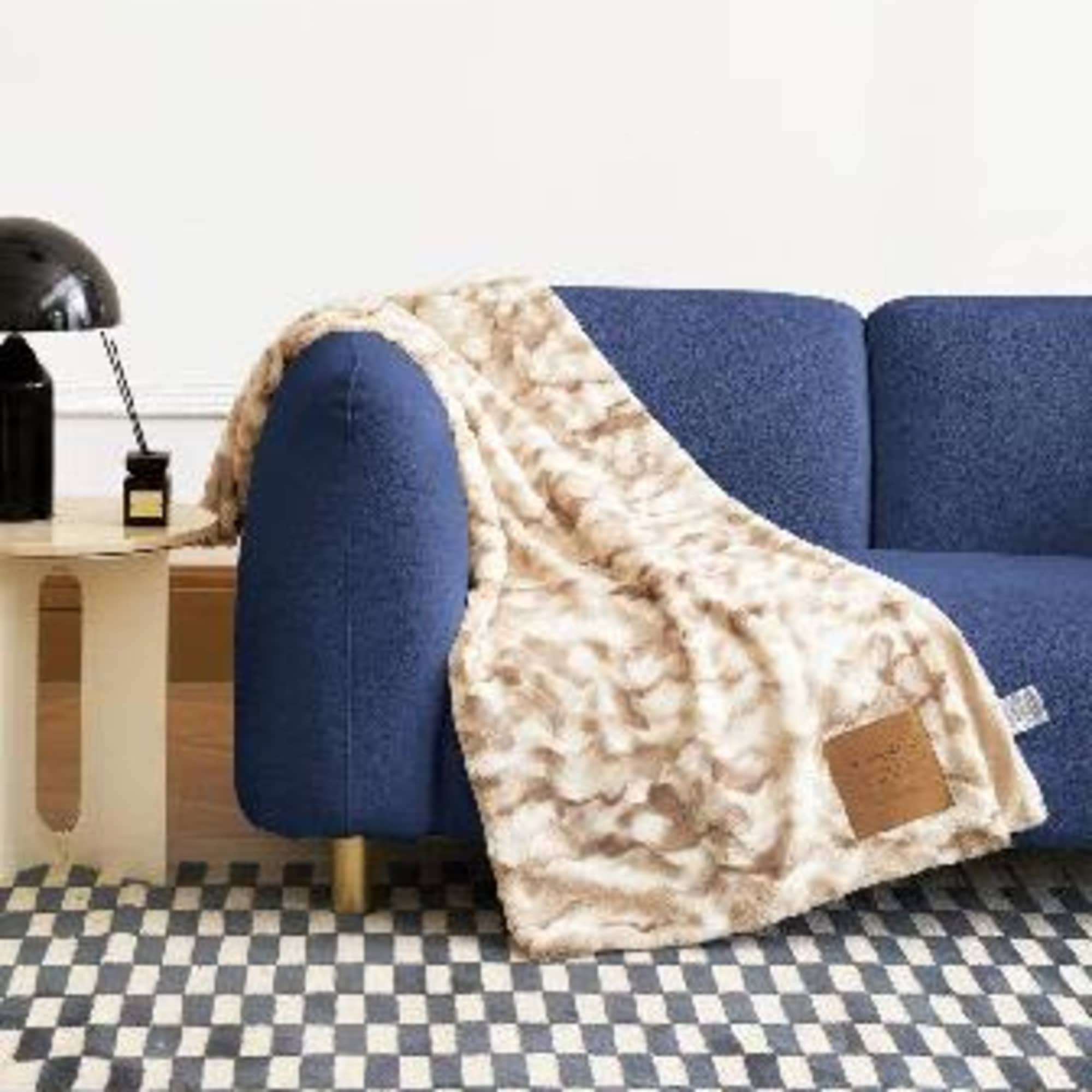 Patterned throw blanket draped over a blue sofa beside a side table and lamp