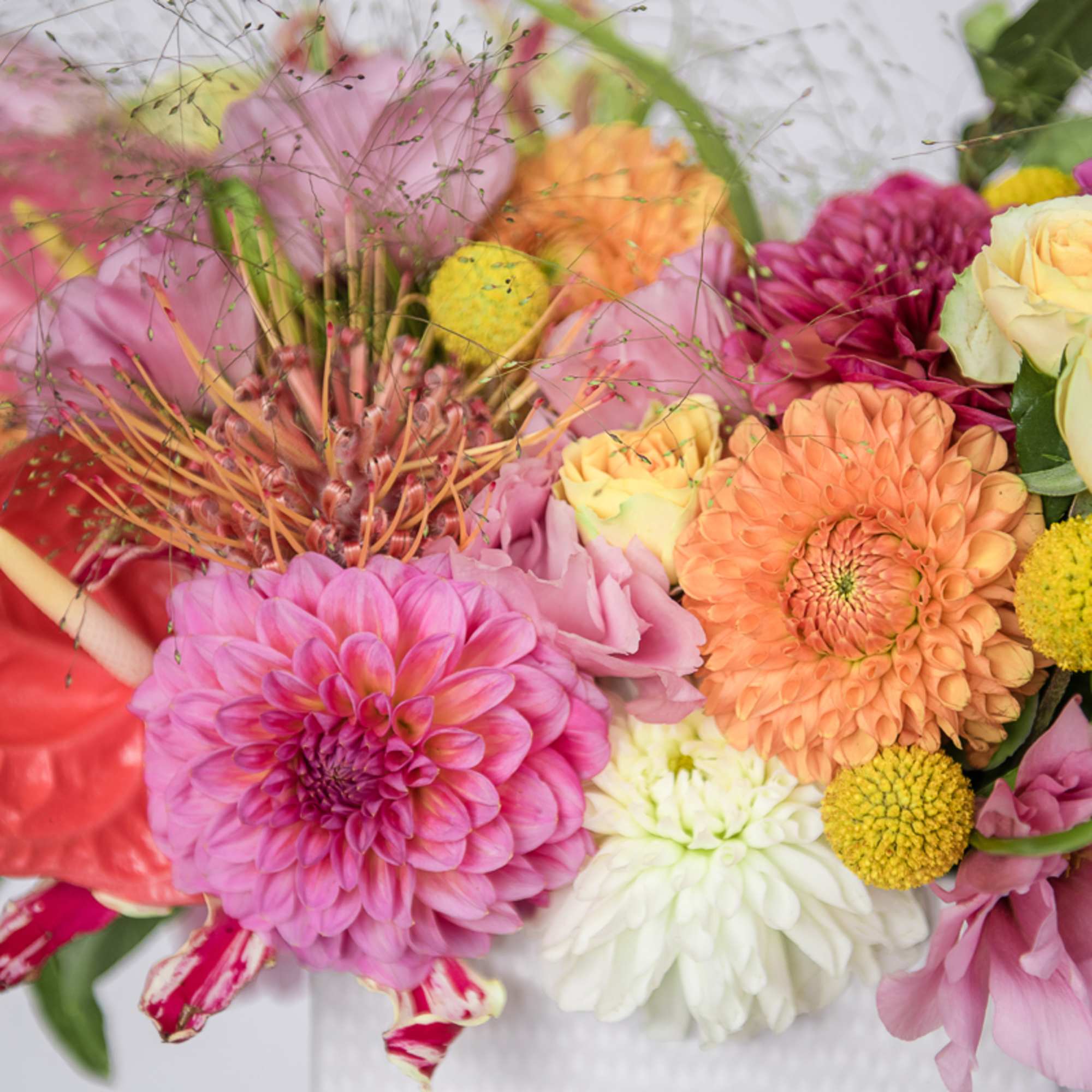 Colorful mixed bouquet with pink and orange dahlias, yellow accents, roses, and protea blooms.
