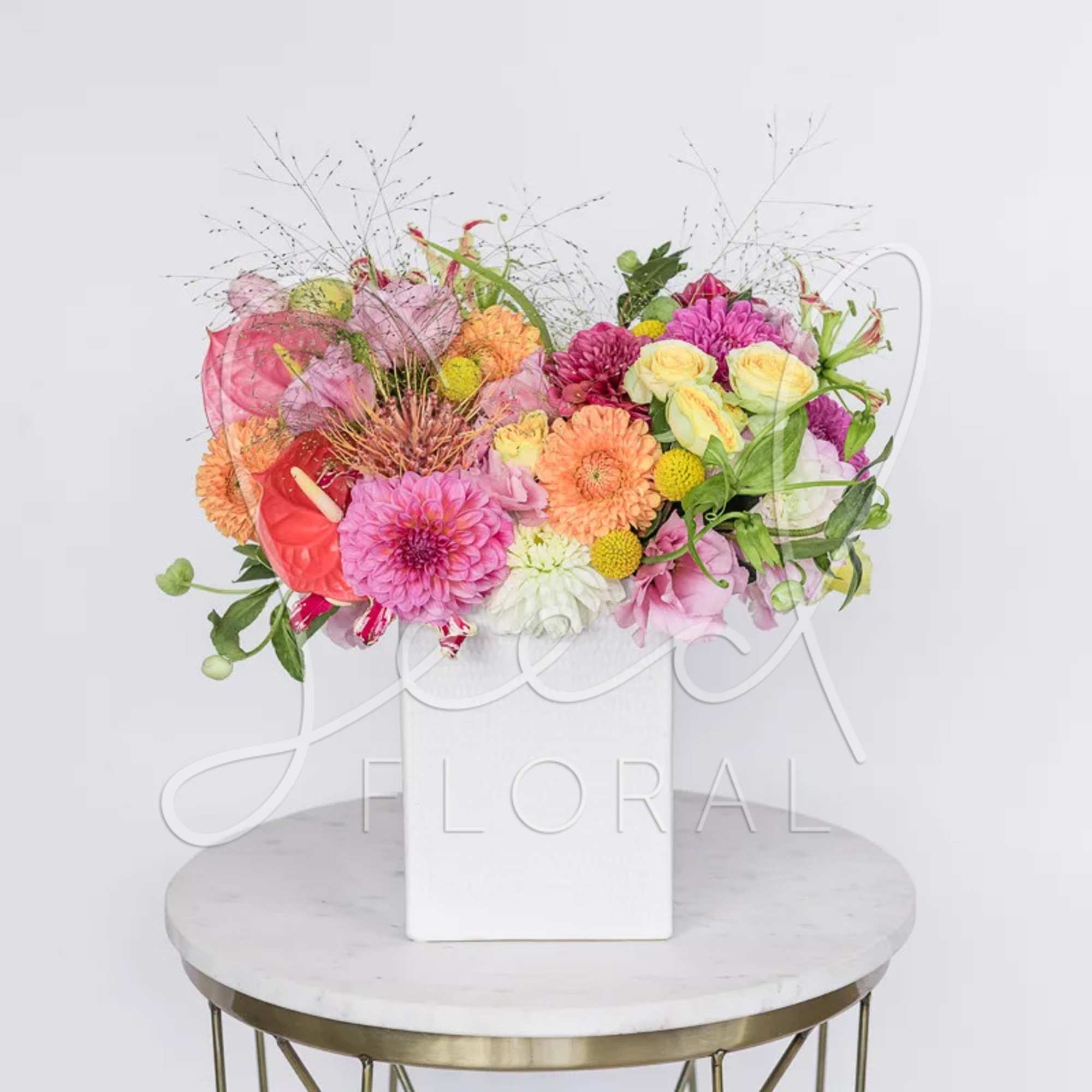 Bright mixed arrangement of pink, orange, and yellow flowers in a white square vase.