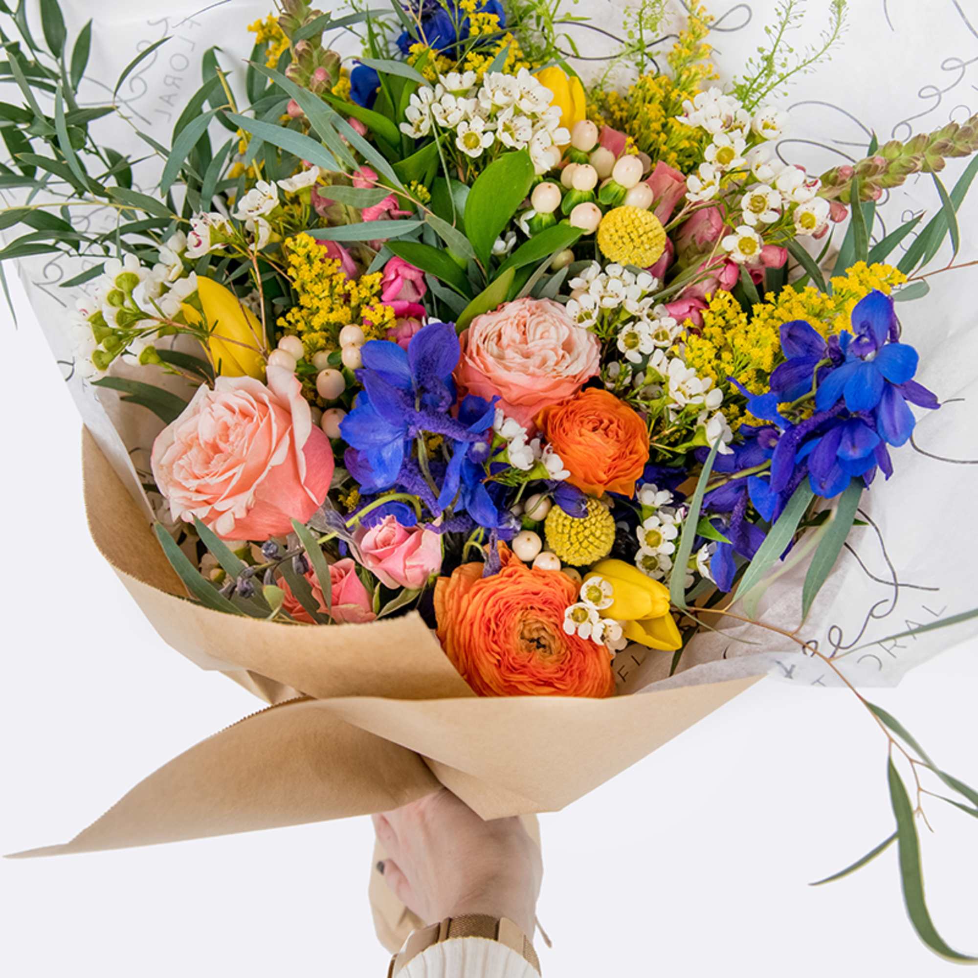 Handheld bouquet of mixed pink, orange, yellow, and blue flowers wrapped in kraft paper