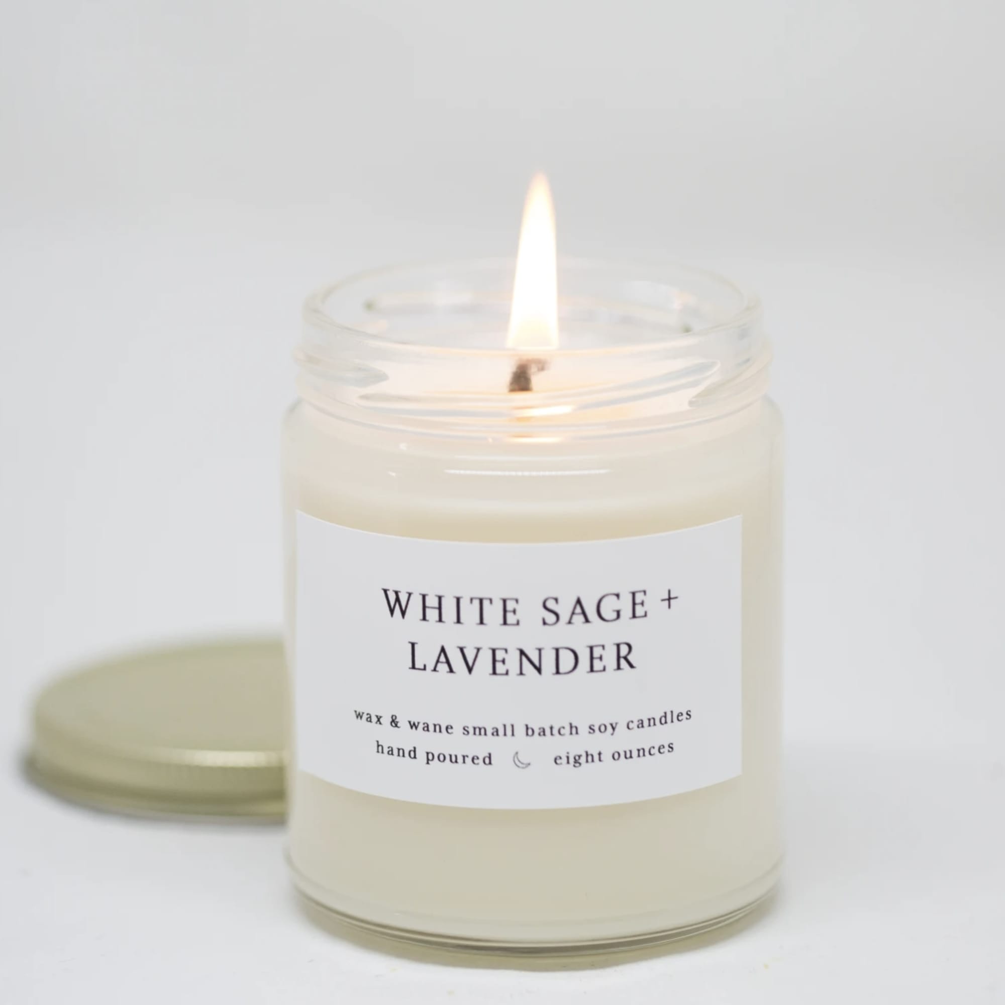Lit white sage and lavender candle in a glass jar with a lid behind it
