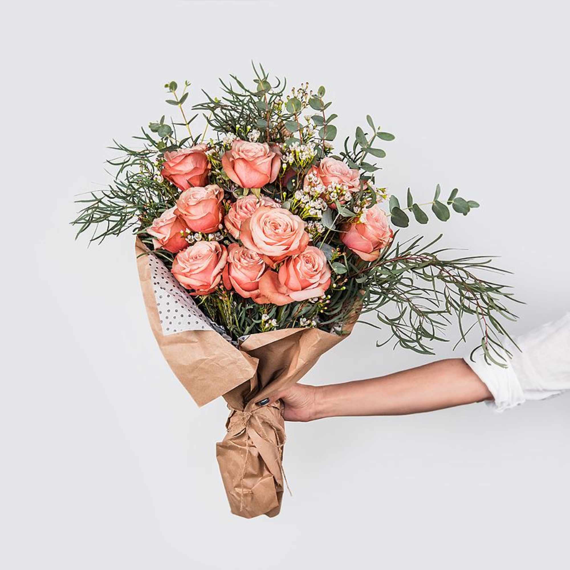 Handheld bouquet of peach roses with airy greenery in brown paper wrap