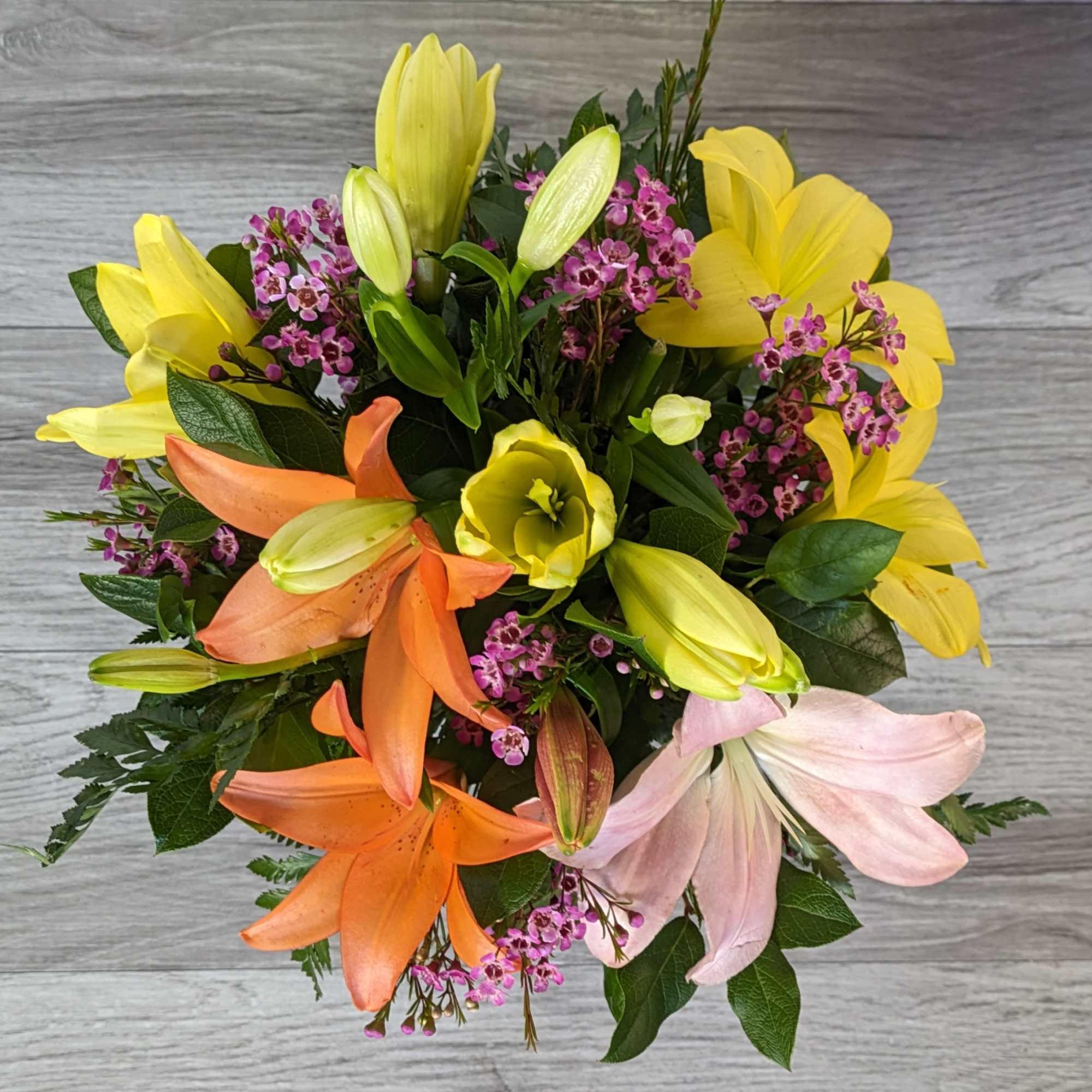 Bouquet of yellow, orange, and pink lilies with small purple filler flowers