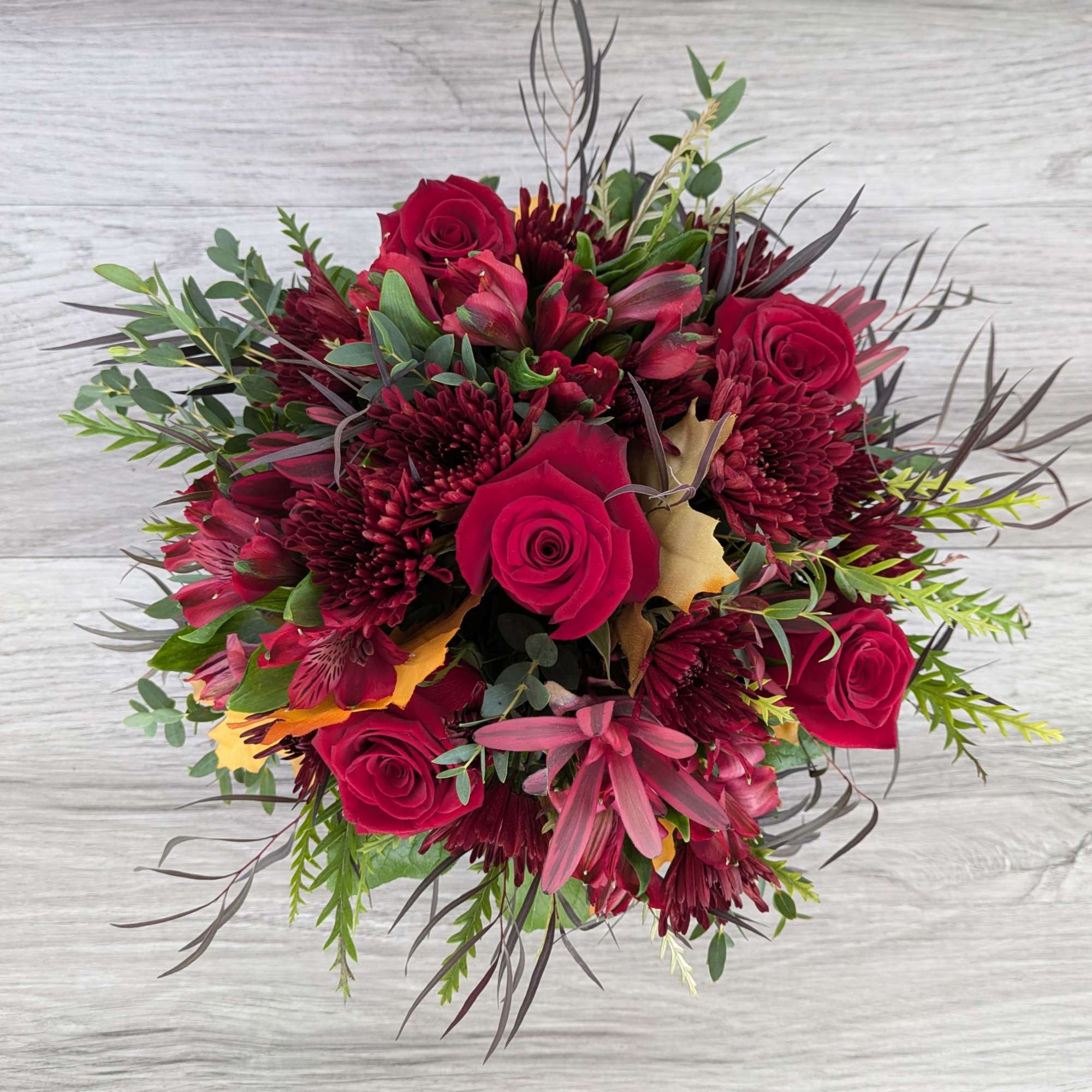 Bouquet of red roses and burgundy flowers with mixed greenery