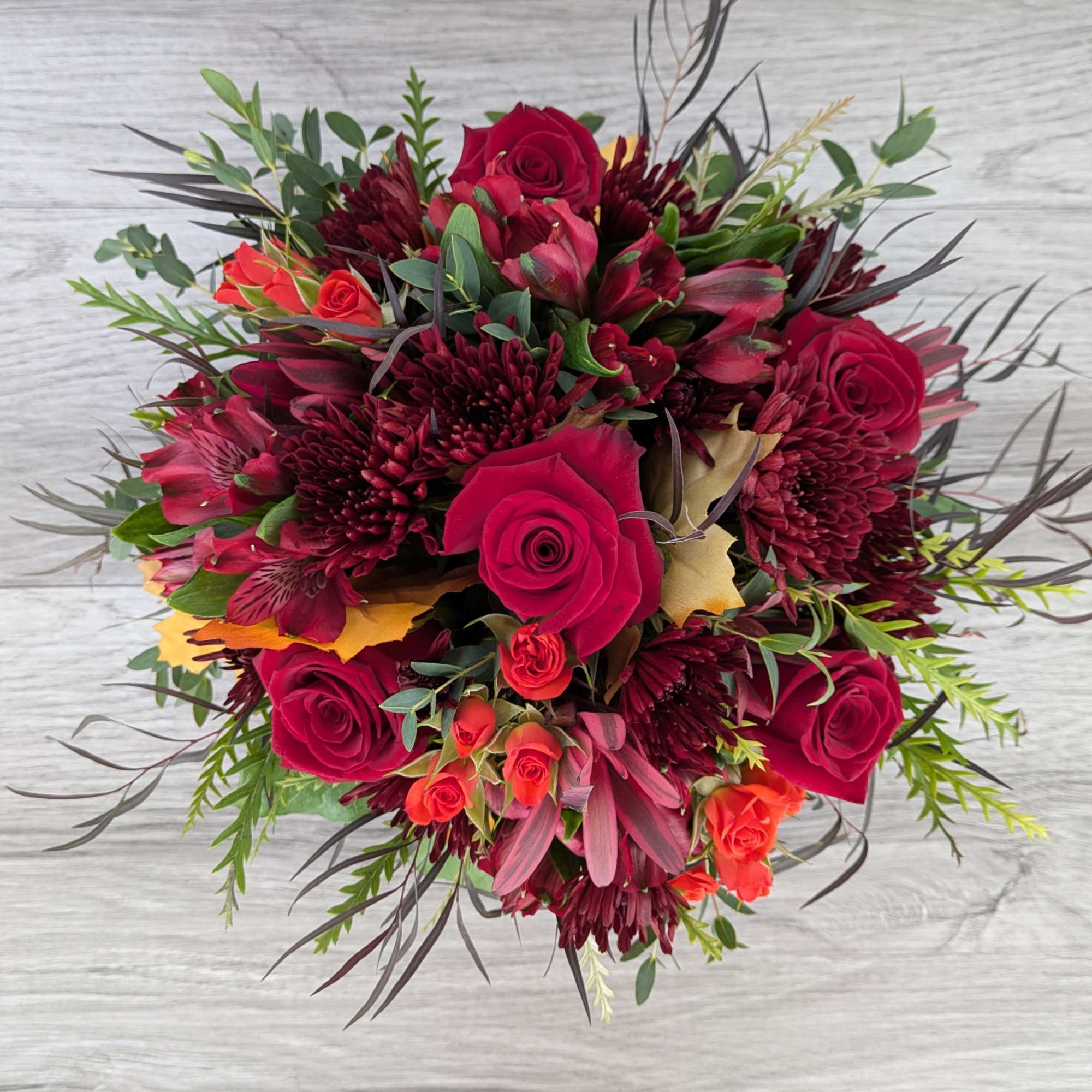 Bouquet of red roses and burgundy flowers with mixed greenery