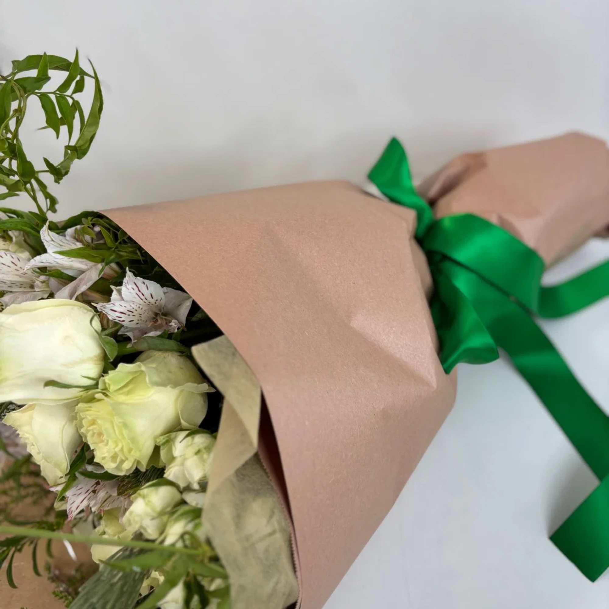 Bouquet of pale cream roses and white striped flowers wrapped in blush paper