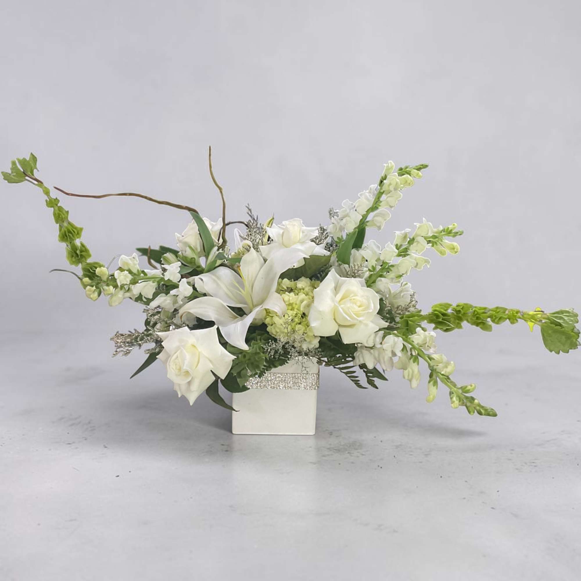 White floral arrangement in a square vase with long arching stems