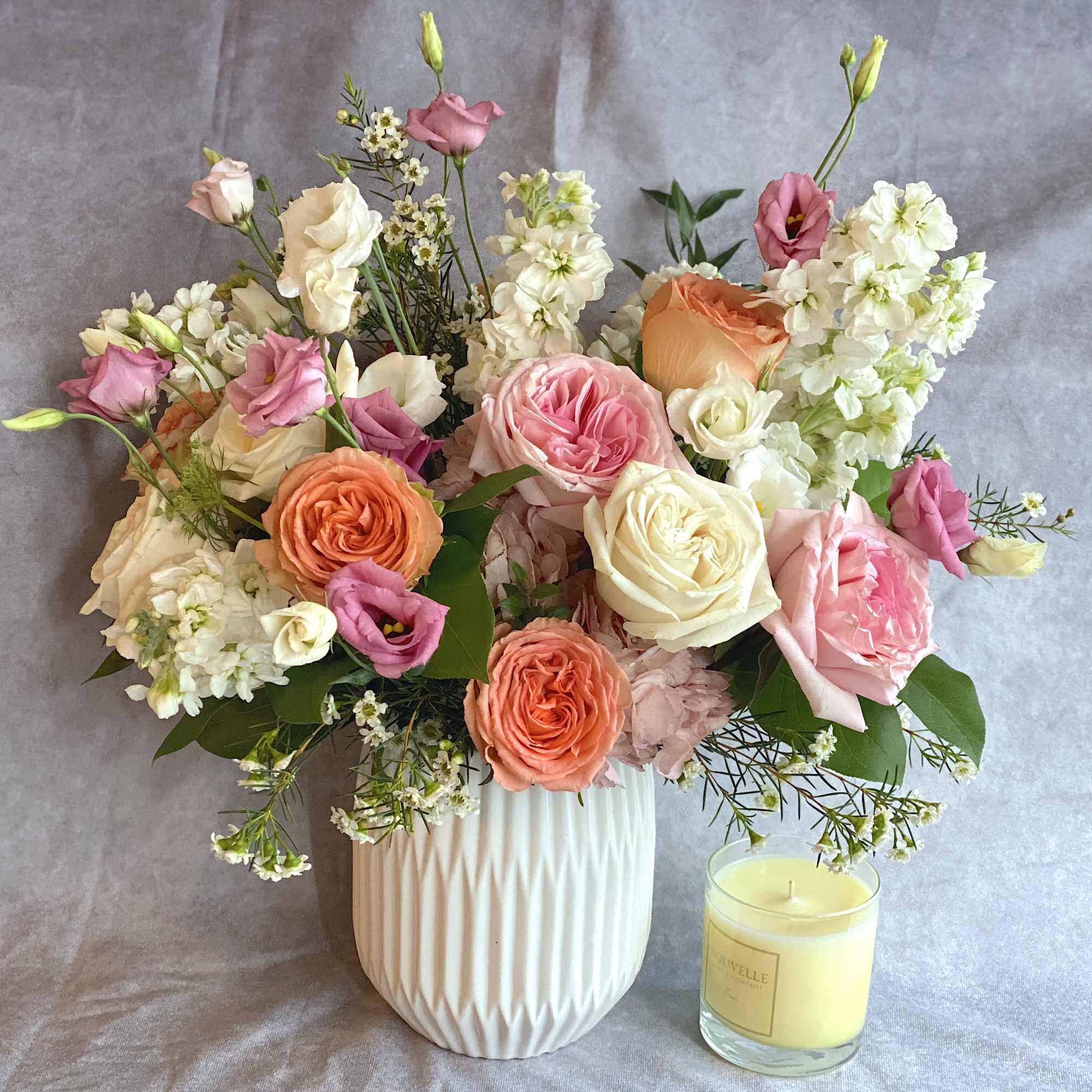 Mixed pink, peach, and white bouquet in a white vase beside a candle