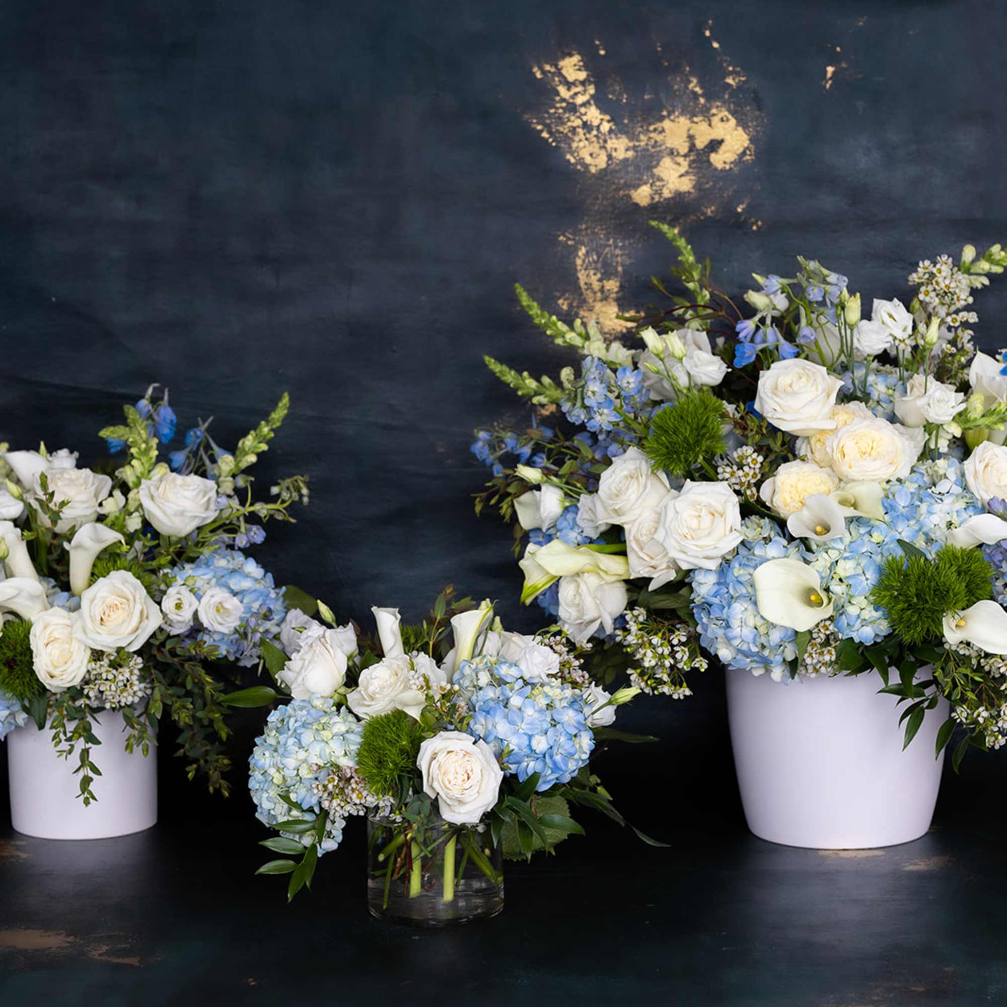 Three blue and white floral arrangements in white containers