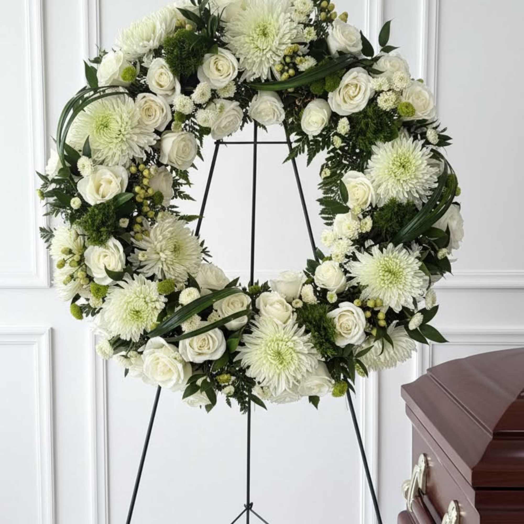 White floral funeral wreath on a black stand beside a casket