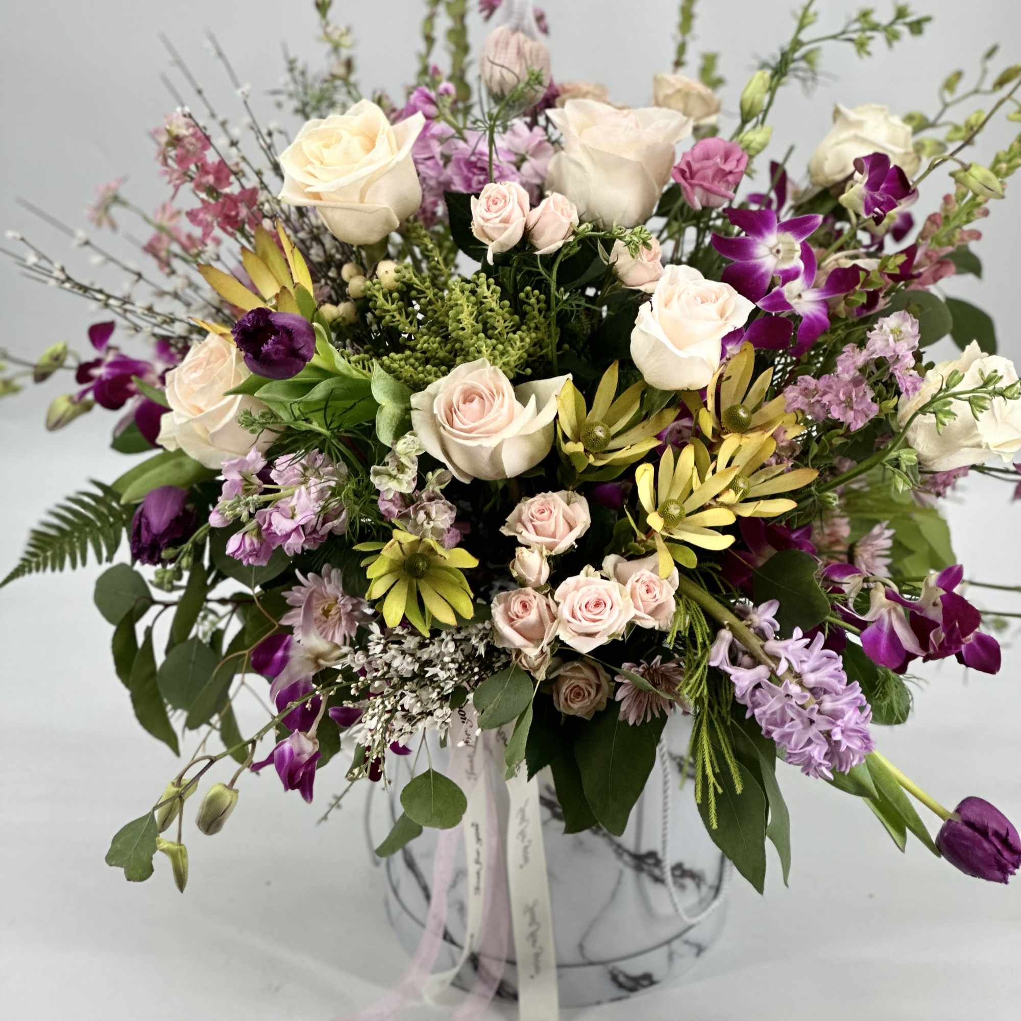 Mixed bouquet of cream roses, purple orchids, and pink blooms in a vase