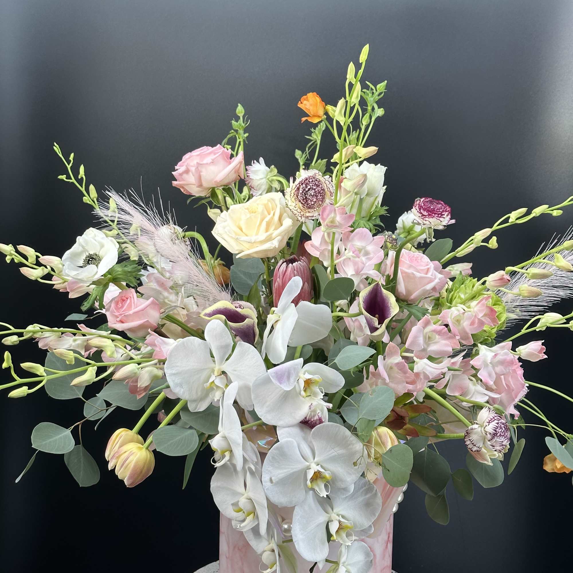 Mixed bouquet with white orchids, pink roses, and pale blooms in a pink box
