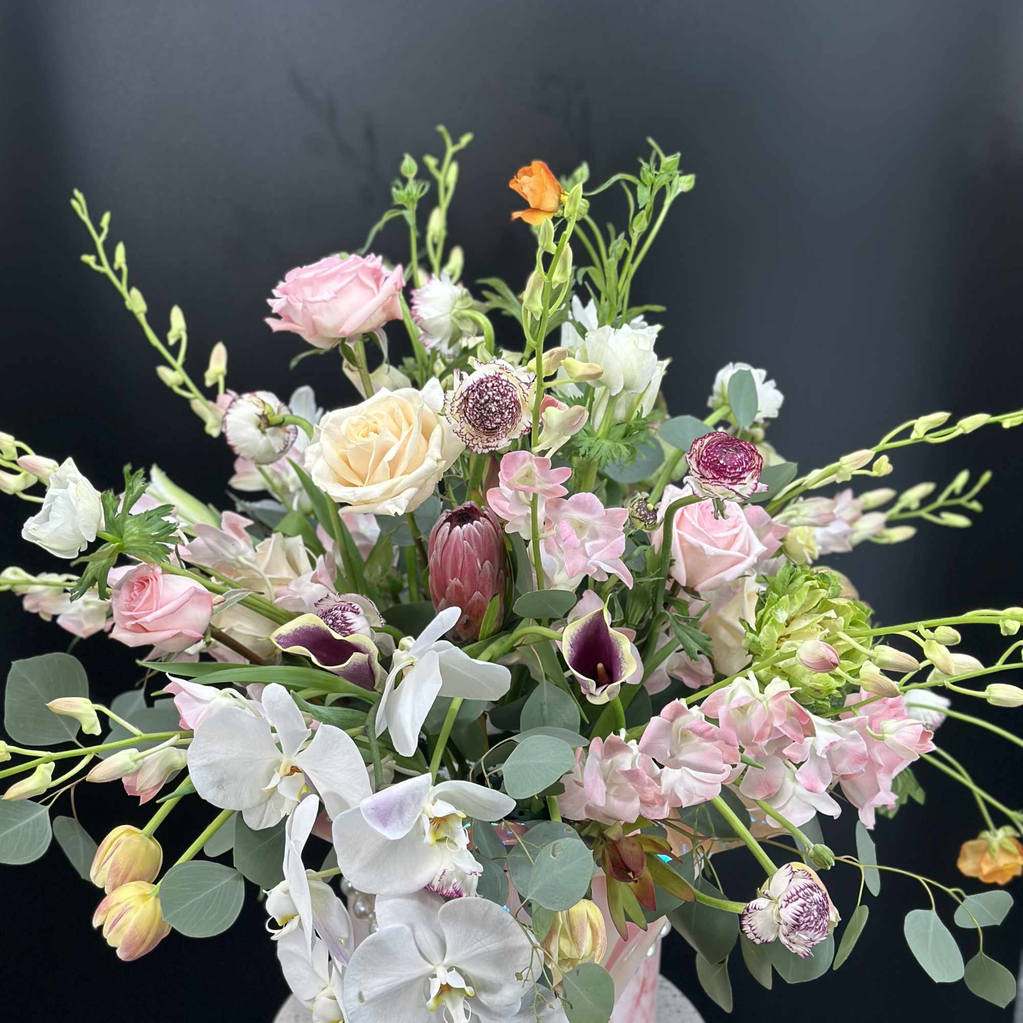 Mixed pastel bouquet with roses, orchids, and calla lilies in a pink vase