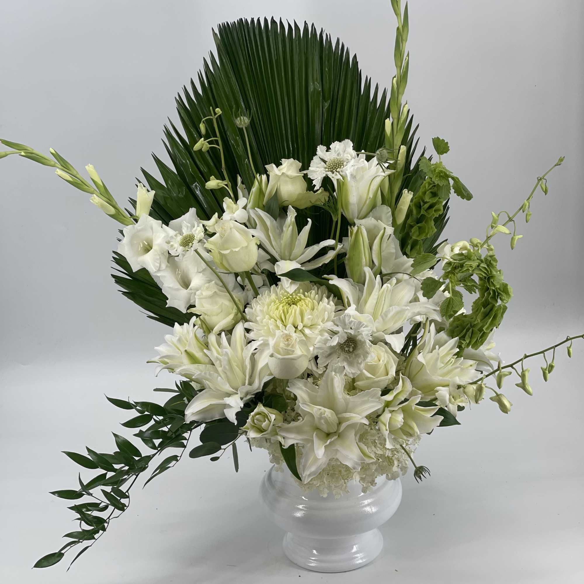 White floral arrangement in a clear glass vase with tall green foliage, photo 4 of 4