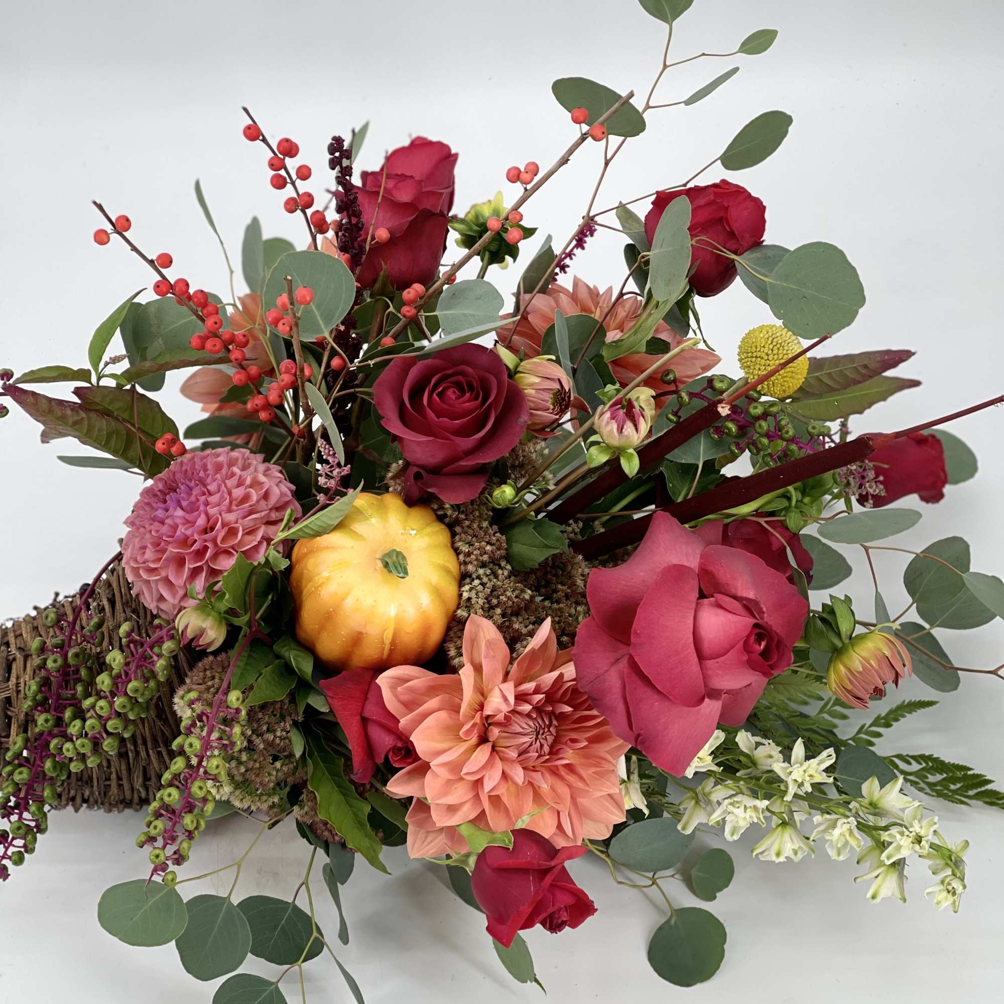 Mixed bouquet with roses, dahlias, and berries in a low basket