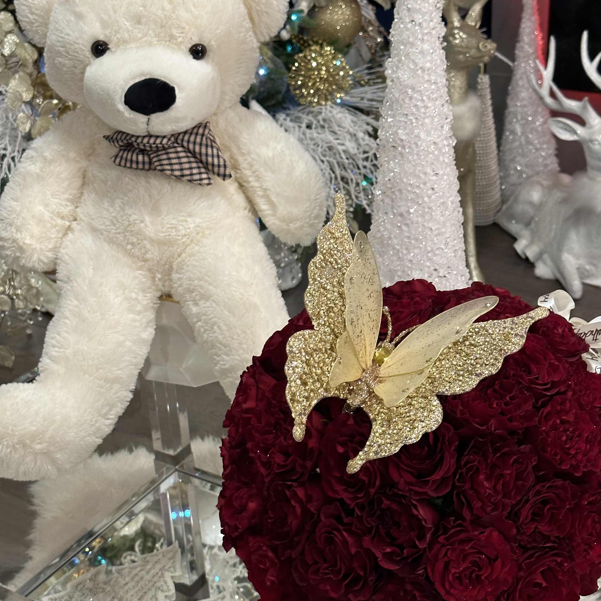 Deep red rose arrangement with a gold butterfly topper beside a white teddy bear