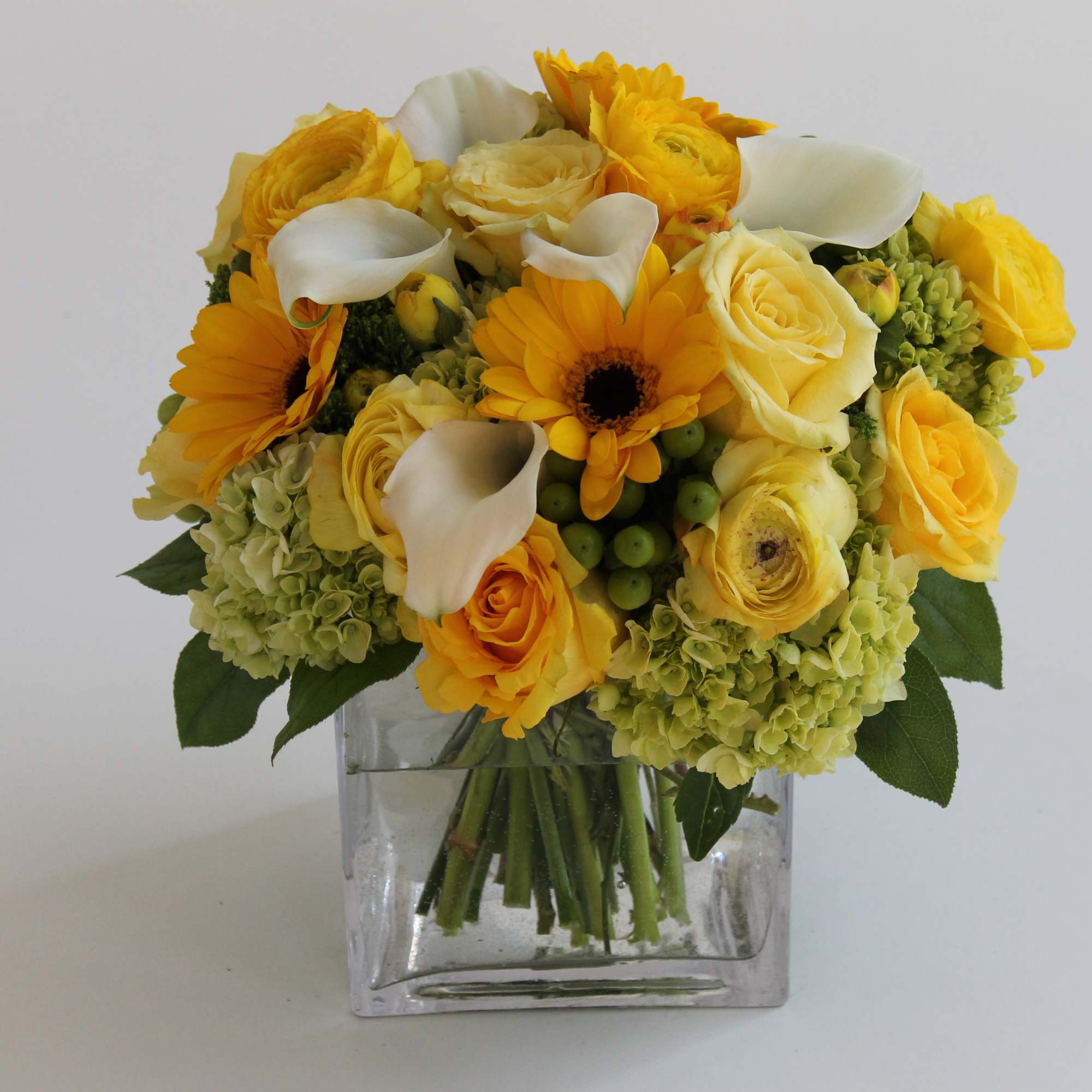Yellow bouquet with roses, calla lilies, and daisies in a clear square vase