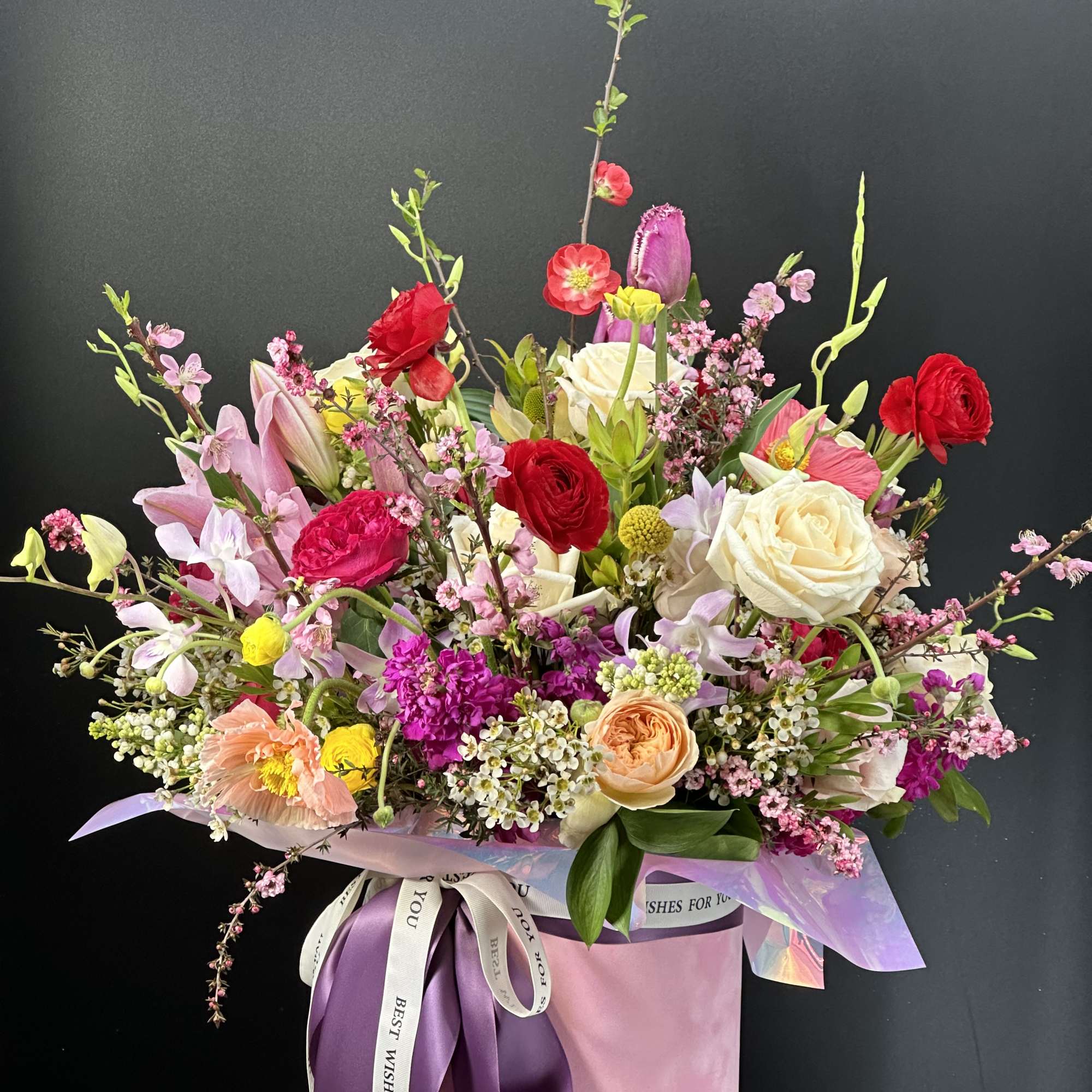 Colorful mixed flower arrangement in a pink hat box with purple ribbon