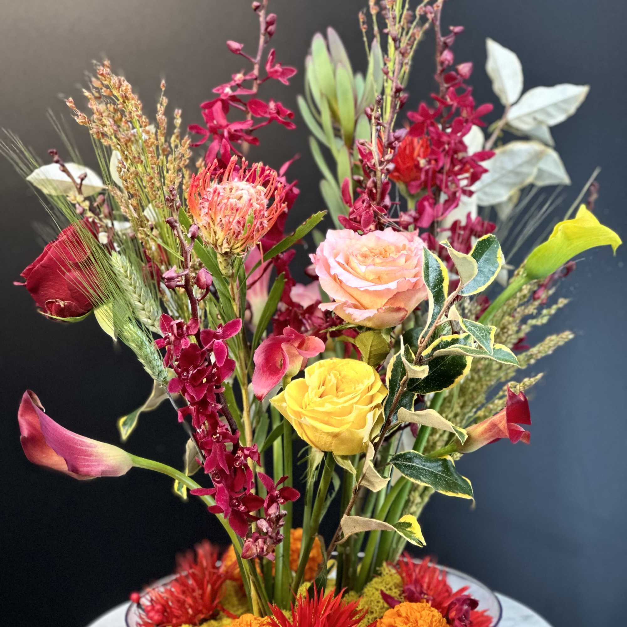 Mixed floral arrangement in a shallow glass bowl with pink, yellow, and red blooms