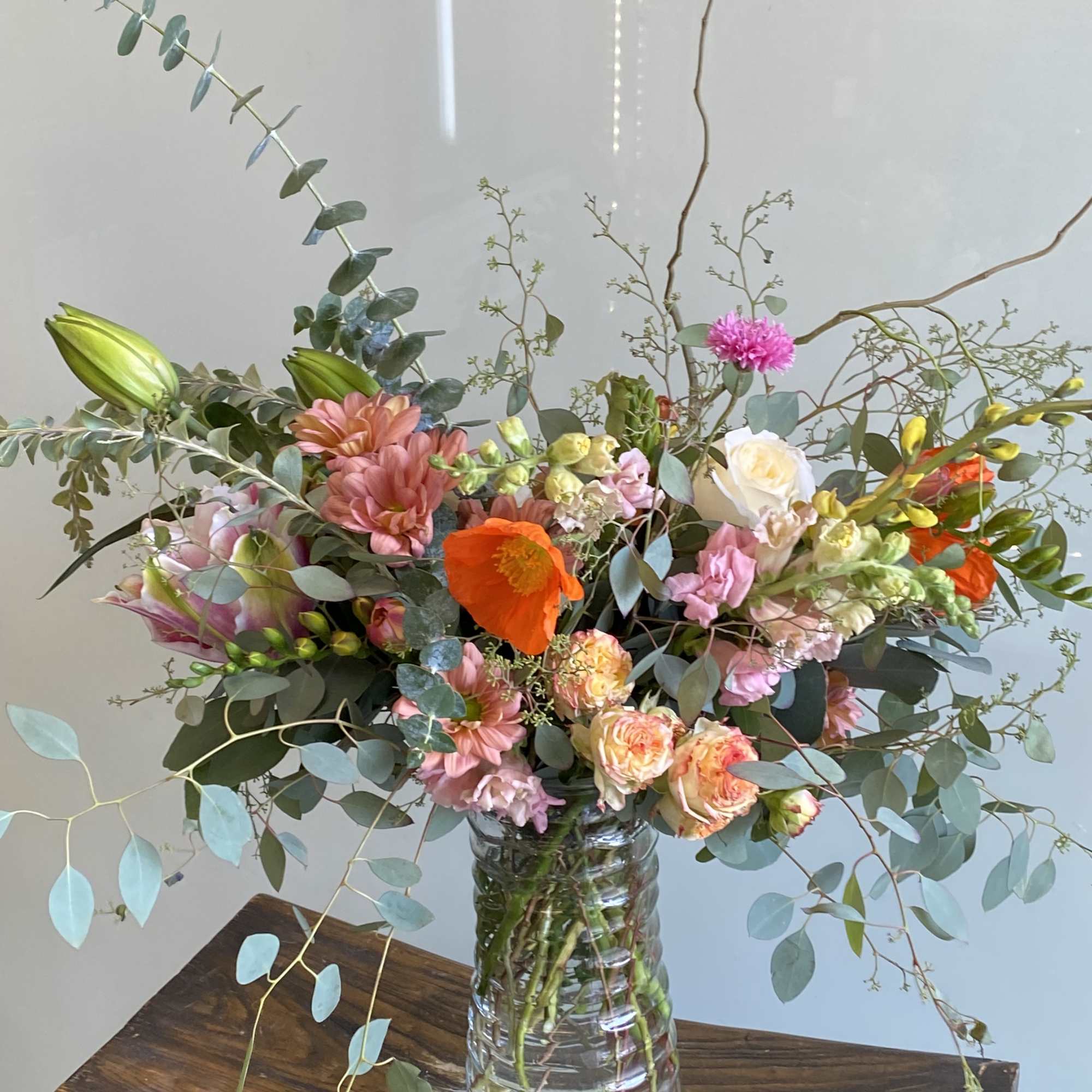 Mixed bouquet of pink, orange, and white flowers in a clear glass vase