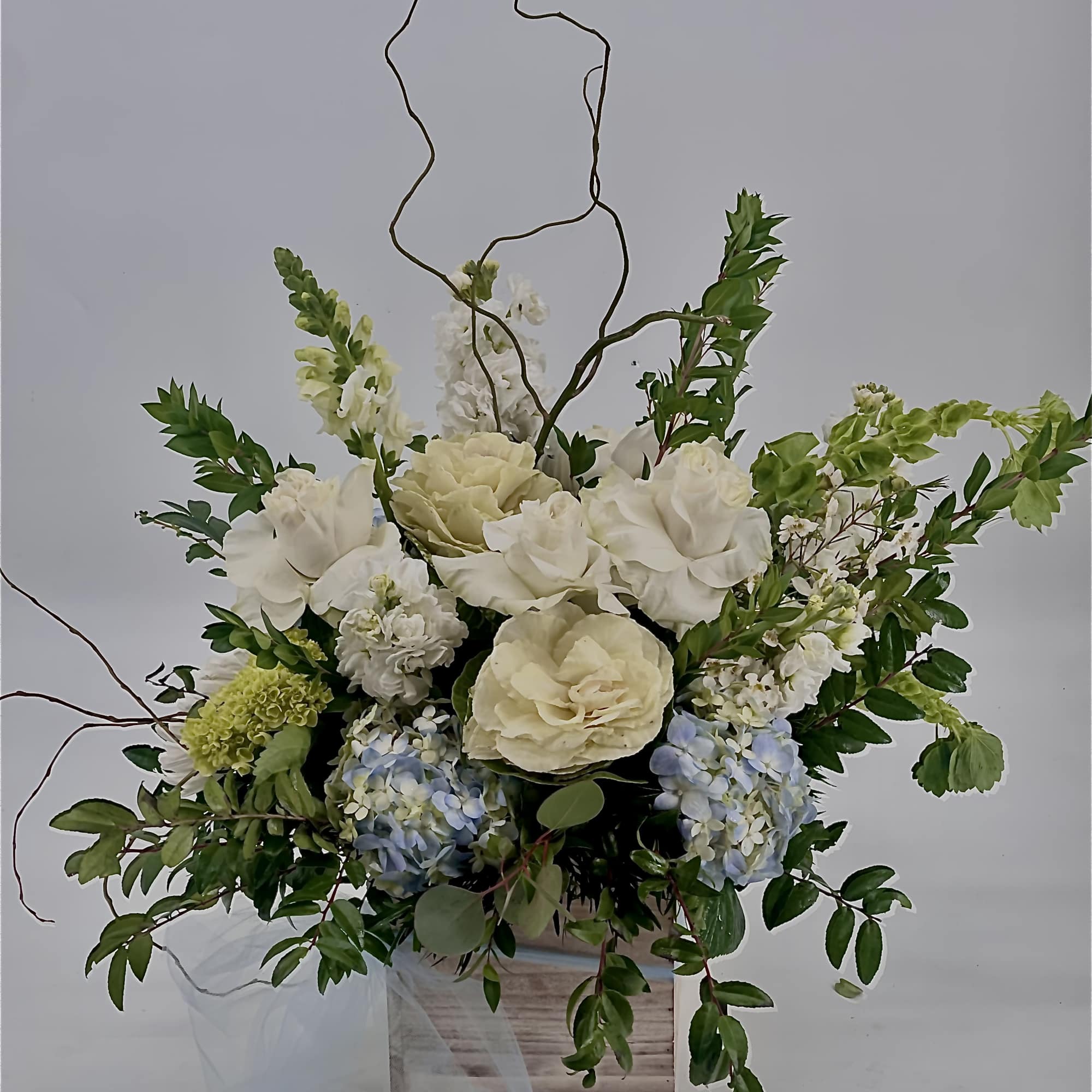 White and pale blue floral arrangement in a wooden box with curly branches