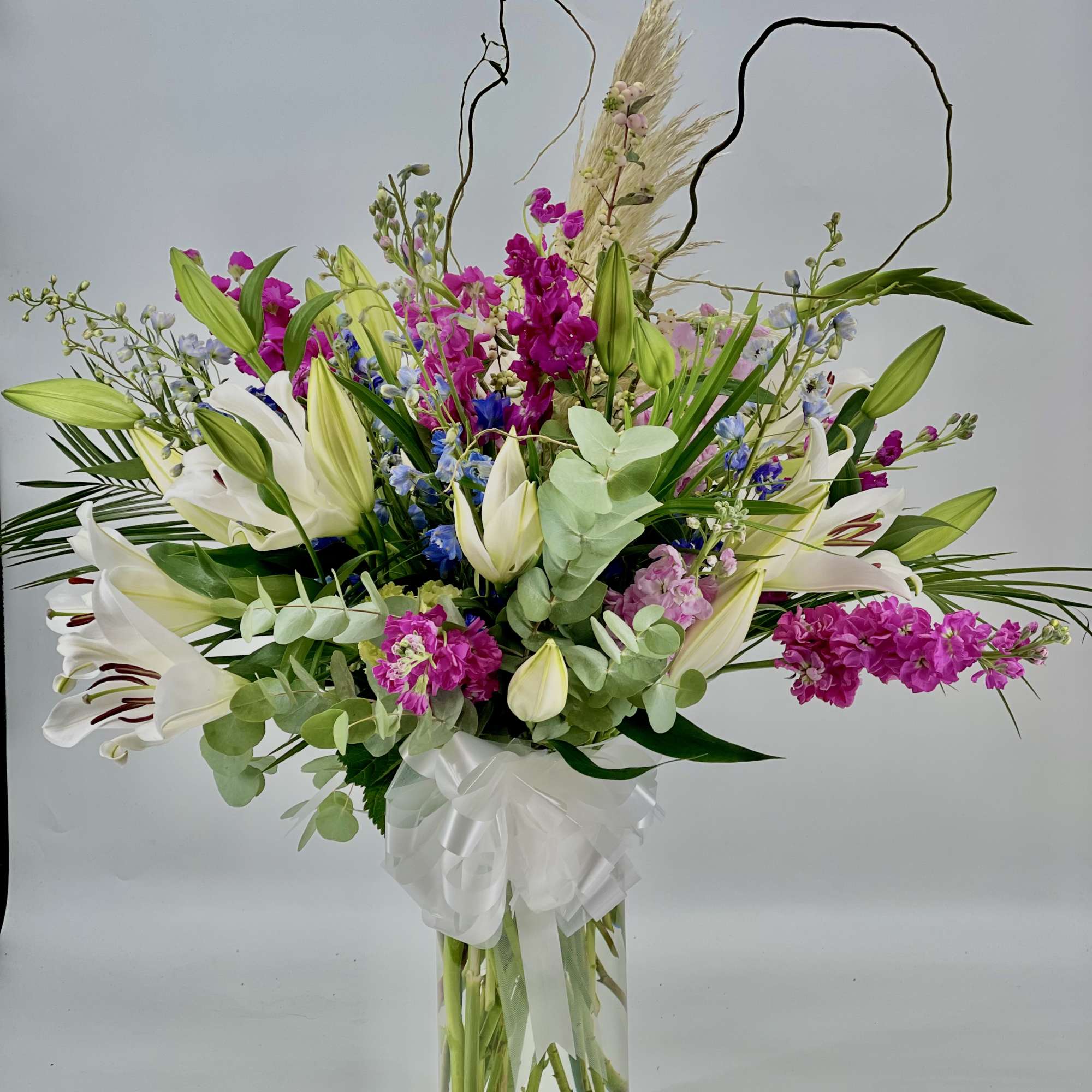 Tall bouquet of white lilies and magenta flowers in a glass vase