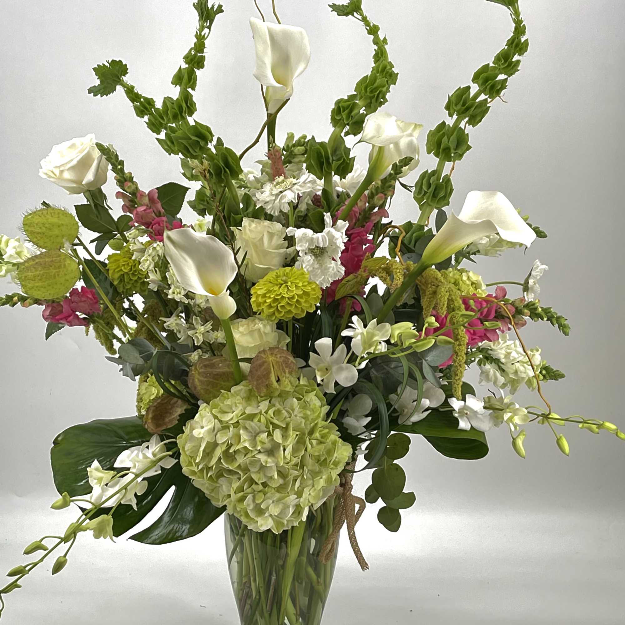 Tall mixed floral arrangement with white calla lilies and green hydrangea in a glass vase