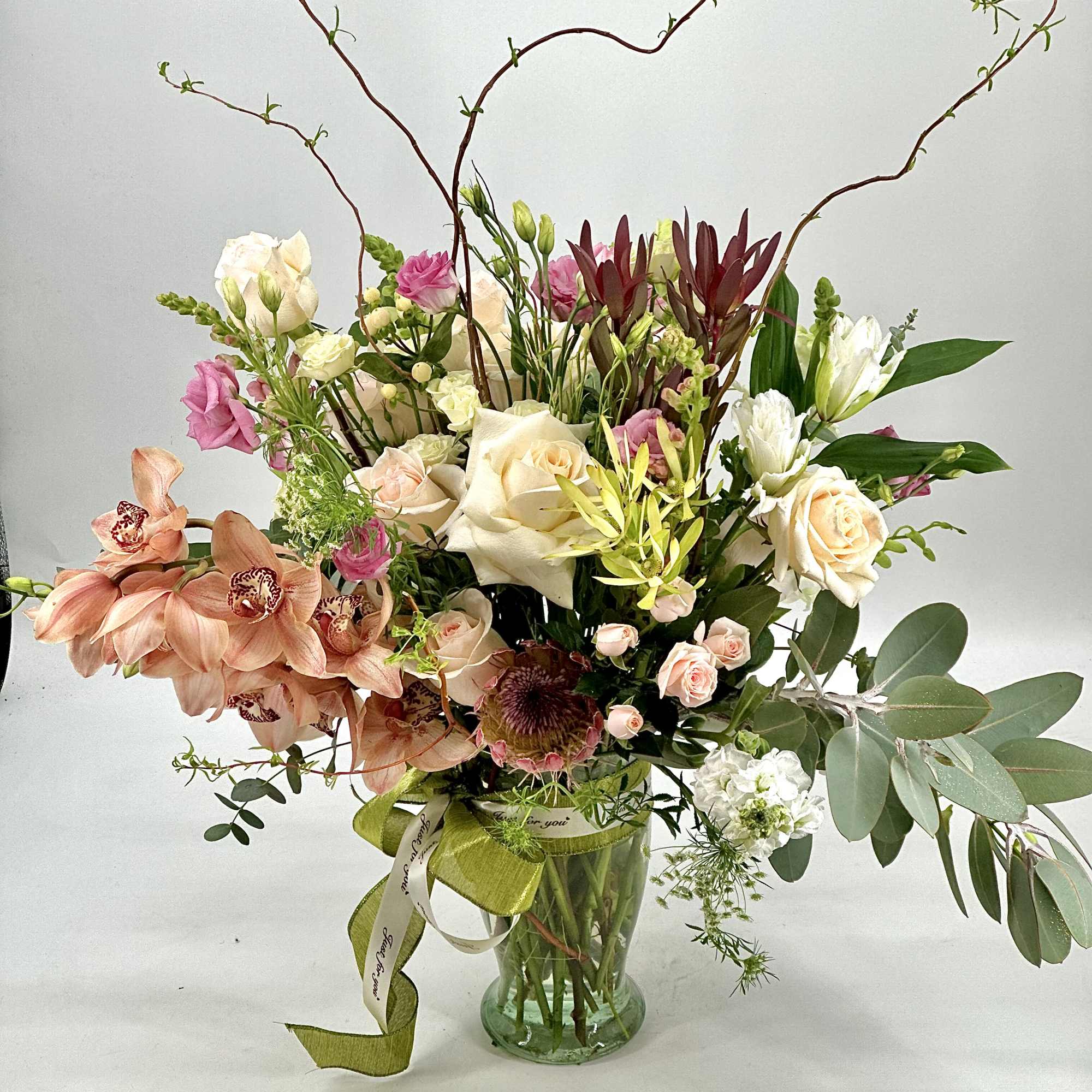 Mixed bouquet in a glass vase with roses, orchids, and branching stems