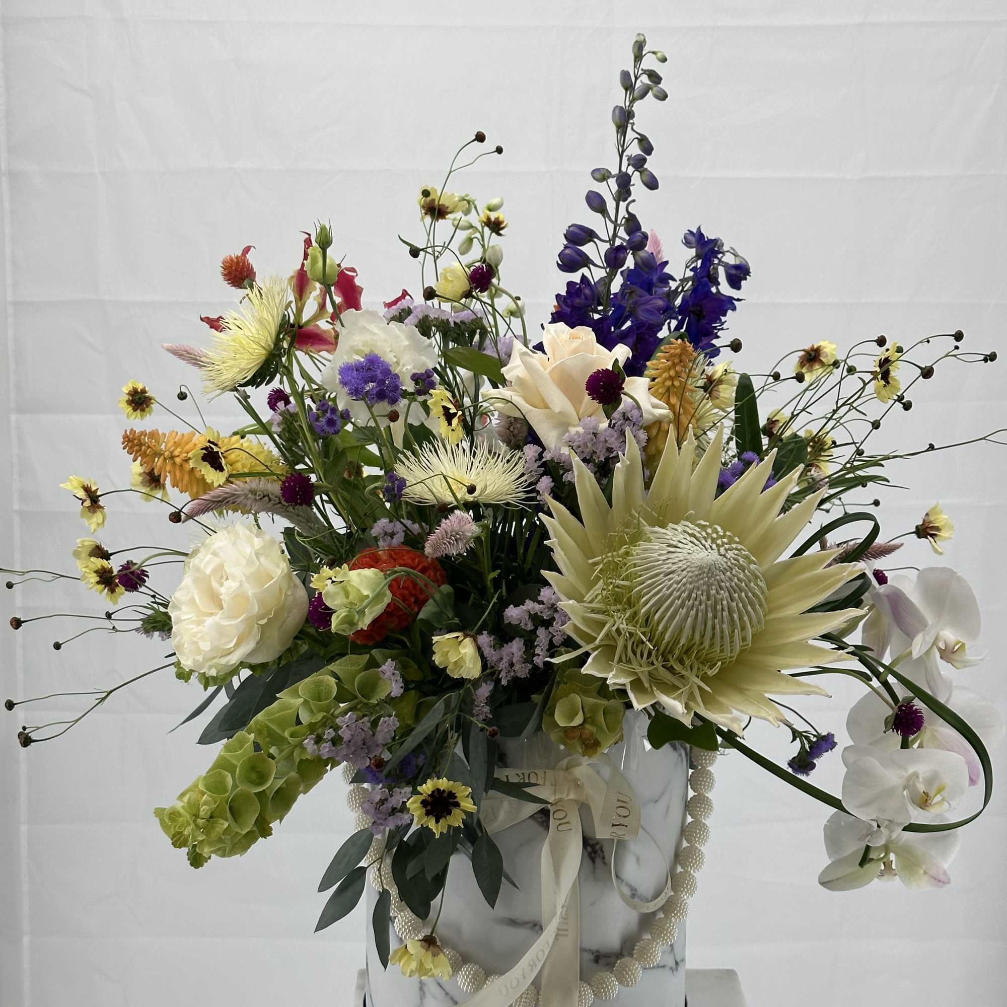 Large mixed flower arrangement in a marble-patterned box with white orchids