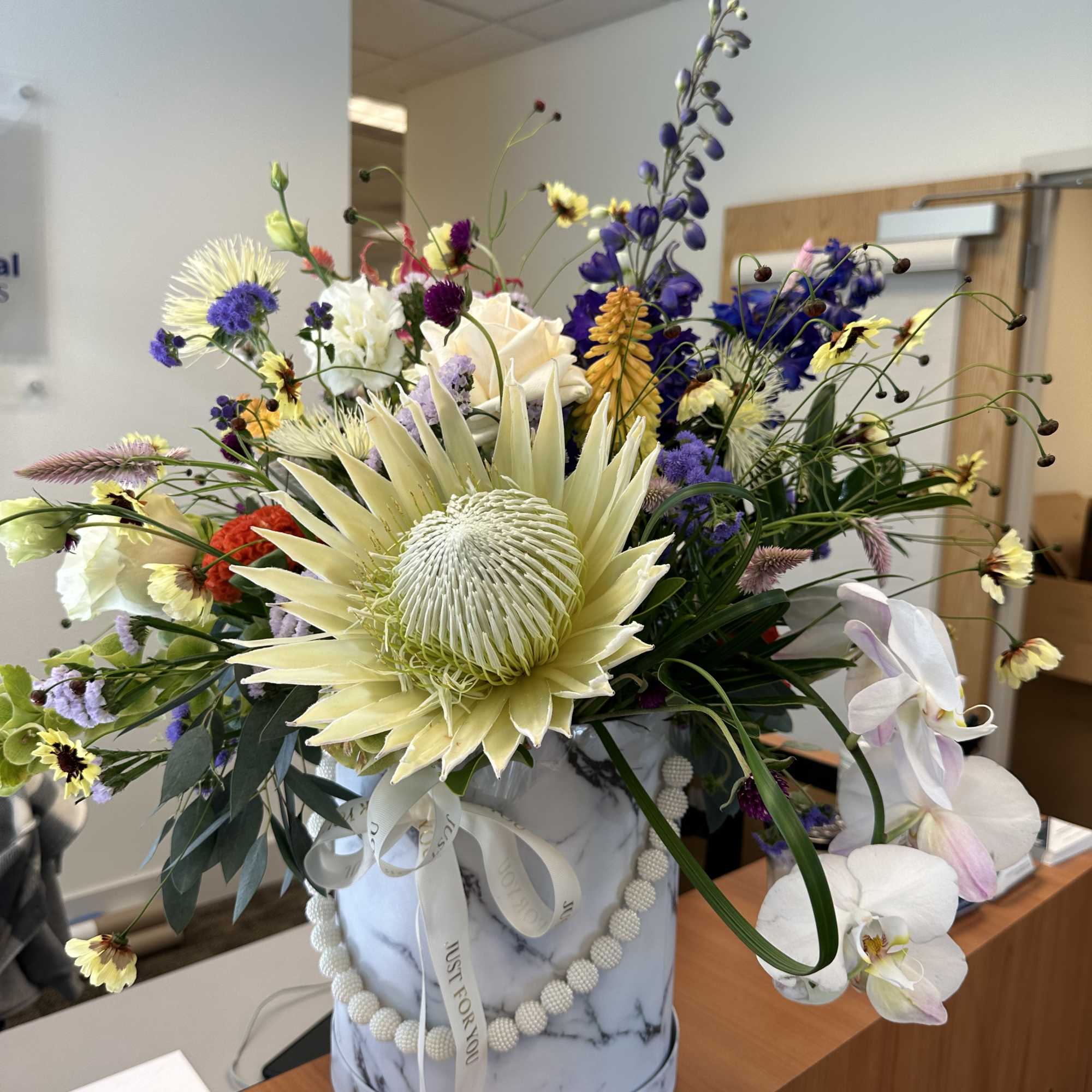 Large mixed flower arrangement in a marble-patterned box with a ribbon