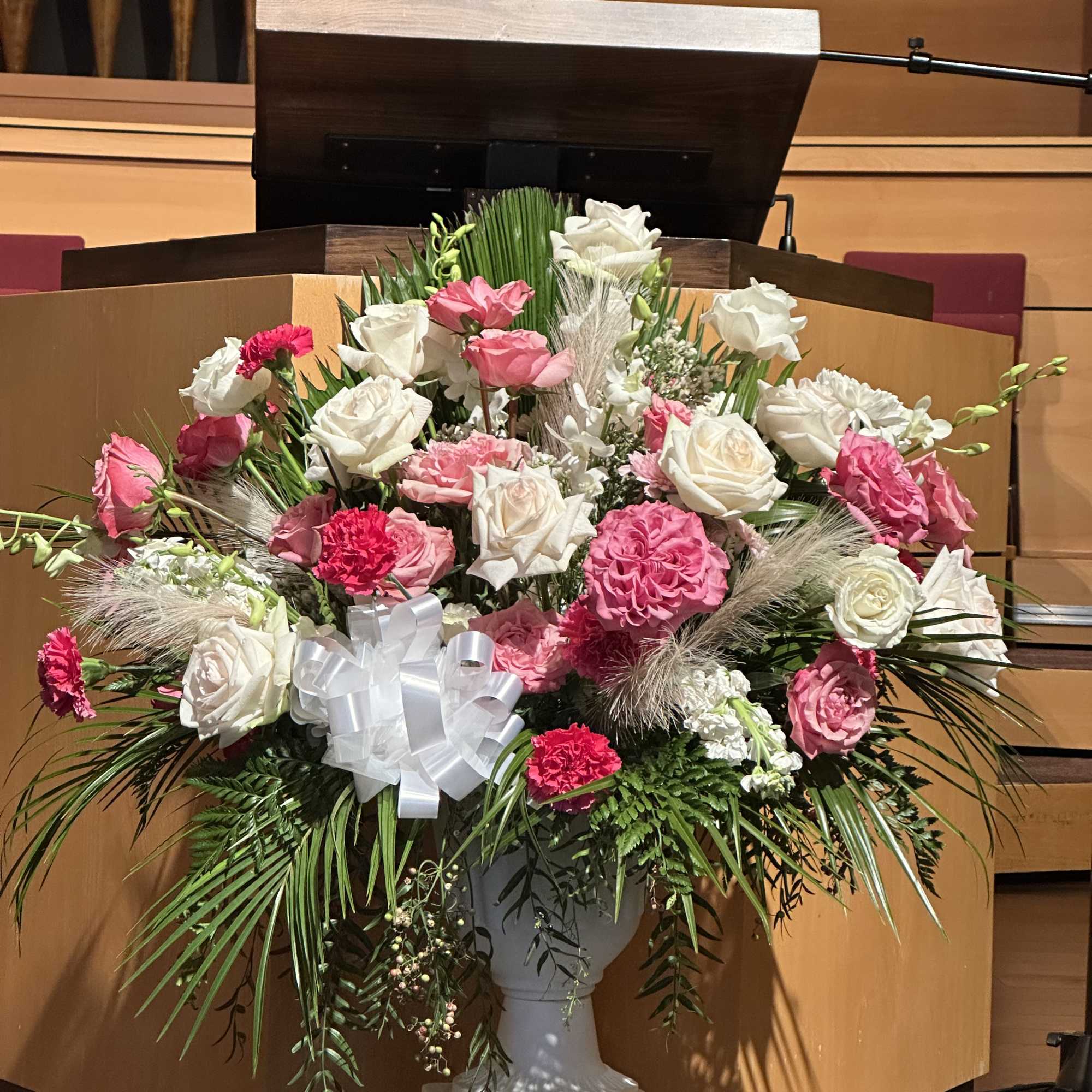 Large pink and white floral arrangement in a white pedestal vase