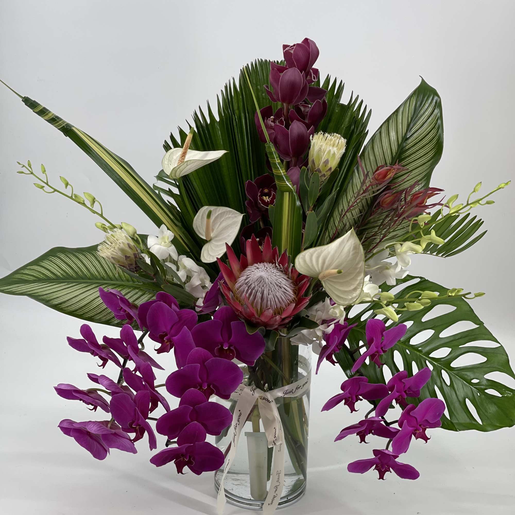 Tropical orchid arrangement in a clear glass vase with large green leaves