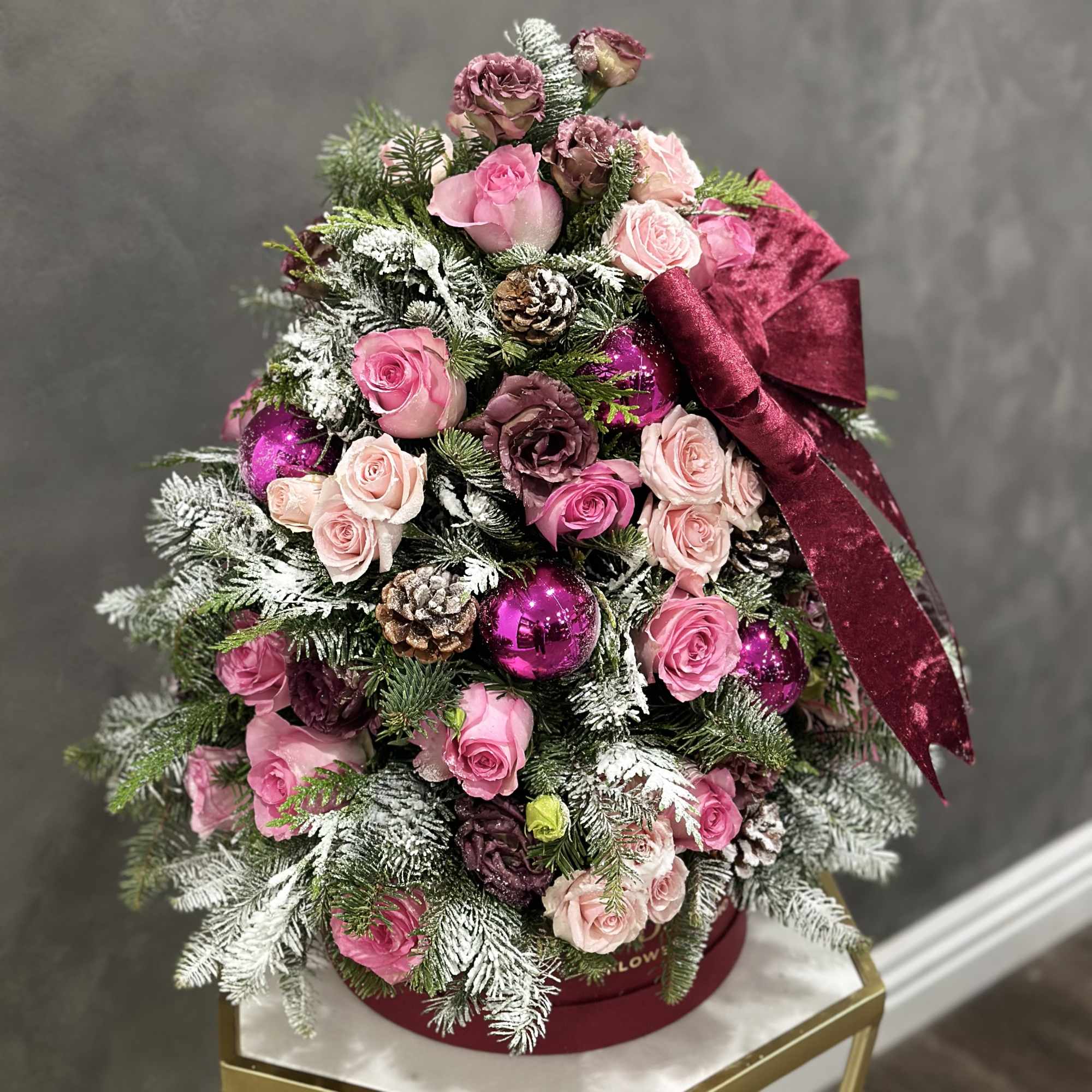 Pink roses and pinecones arranged like a Christmas tree with a burgundy bow