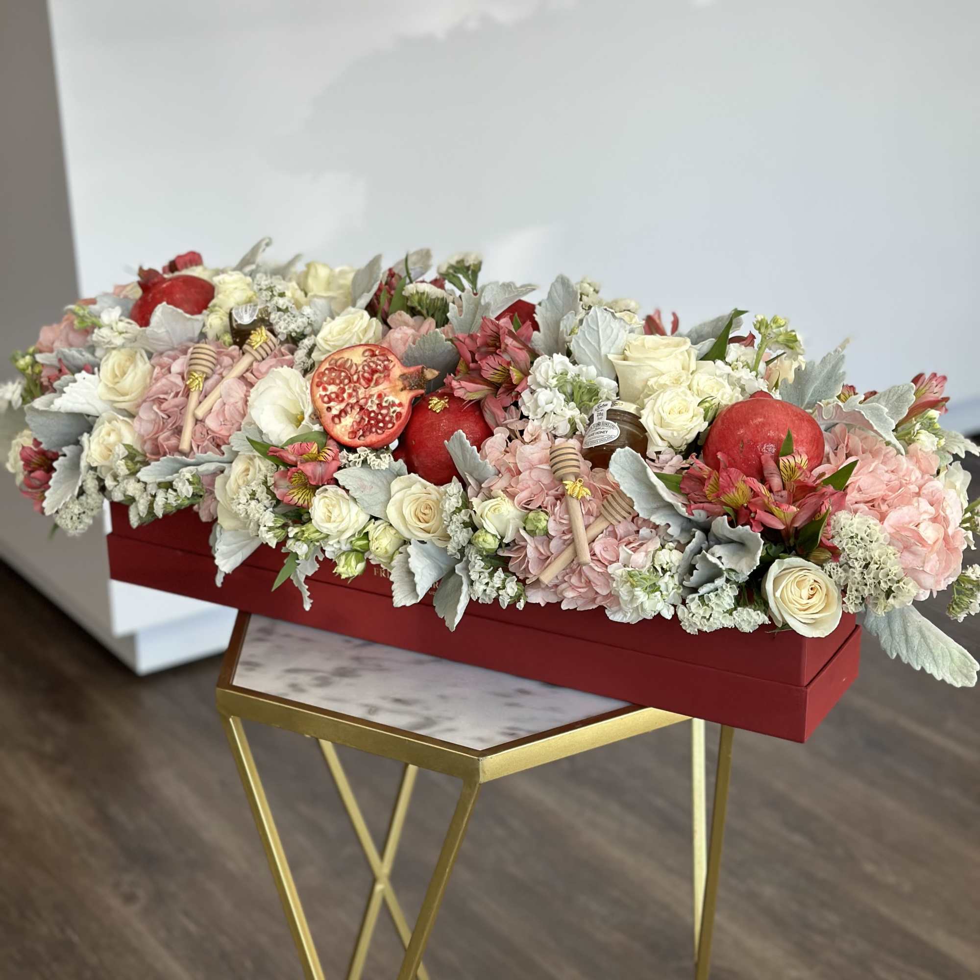 Long floral arrangement with roses, hydrangeas, and pomegranates in a red box