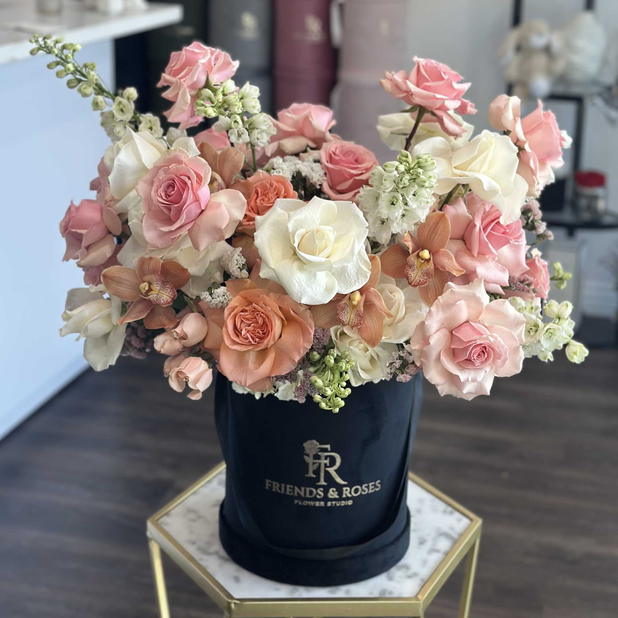 Pink and white roses with orchids in a black hatbox