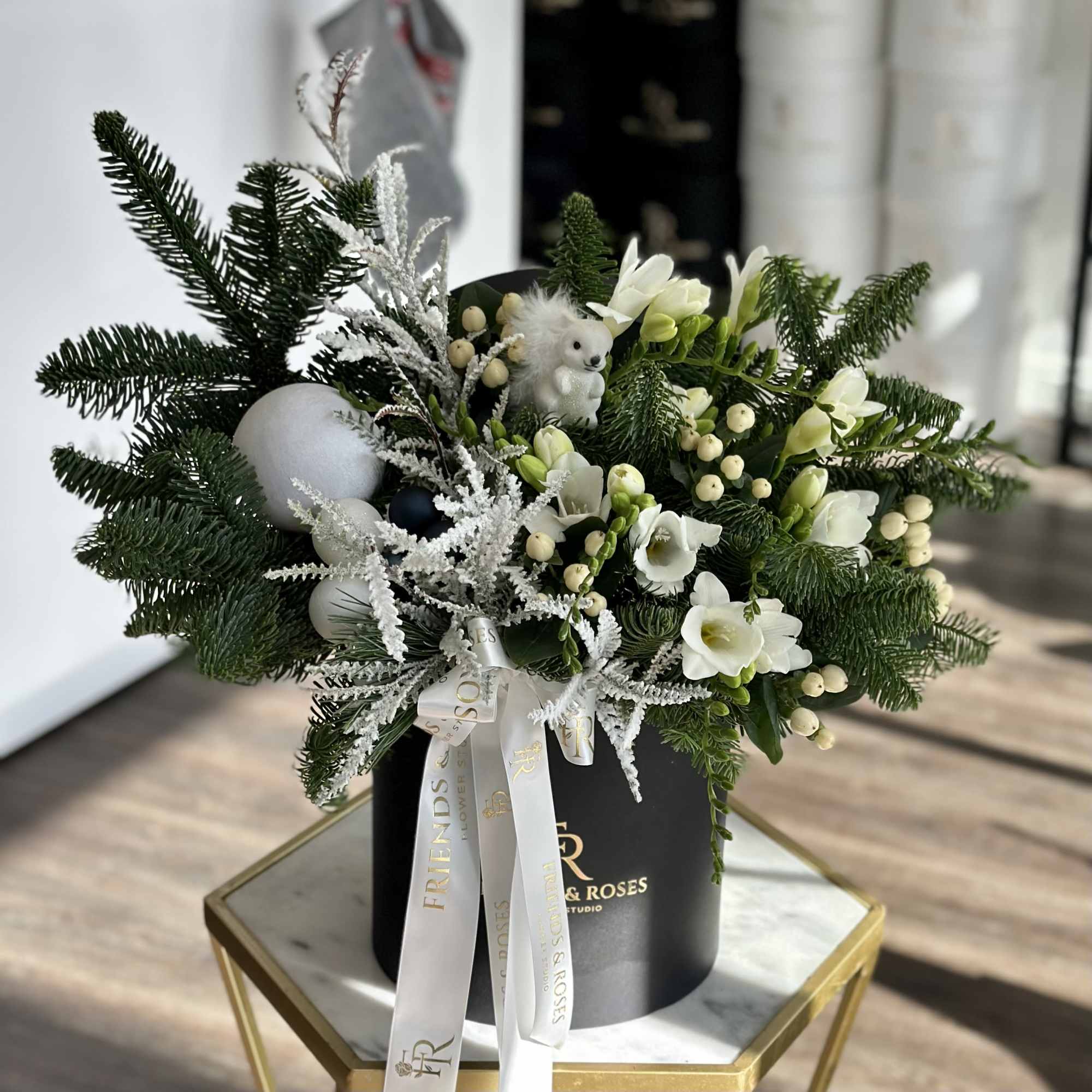 White flowers and evergreen branches arranged in a black hatbox with ribbon